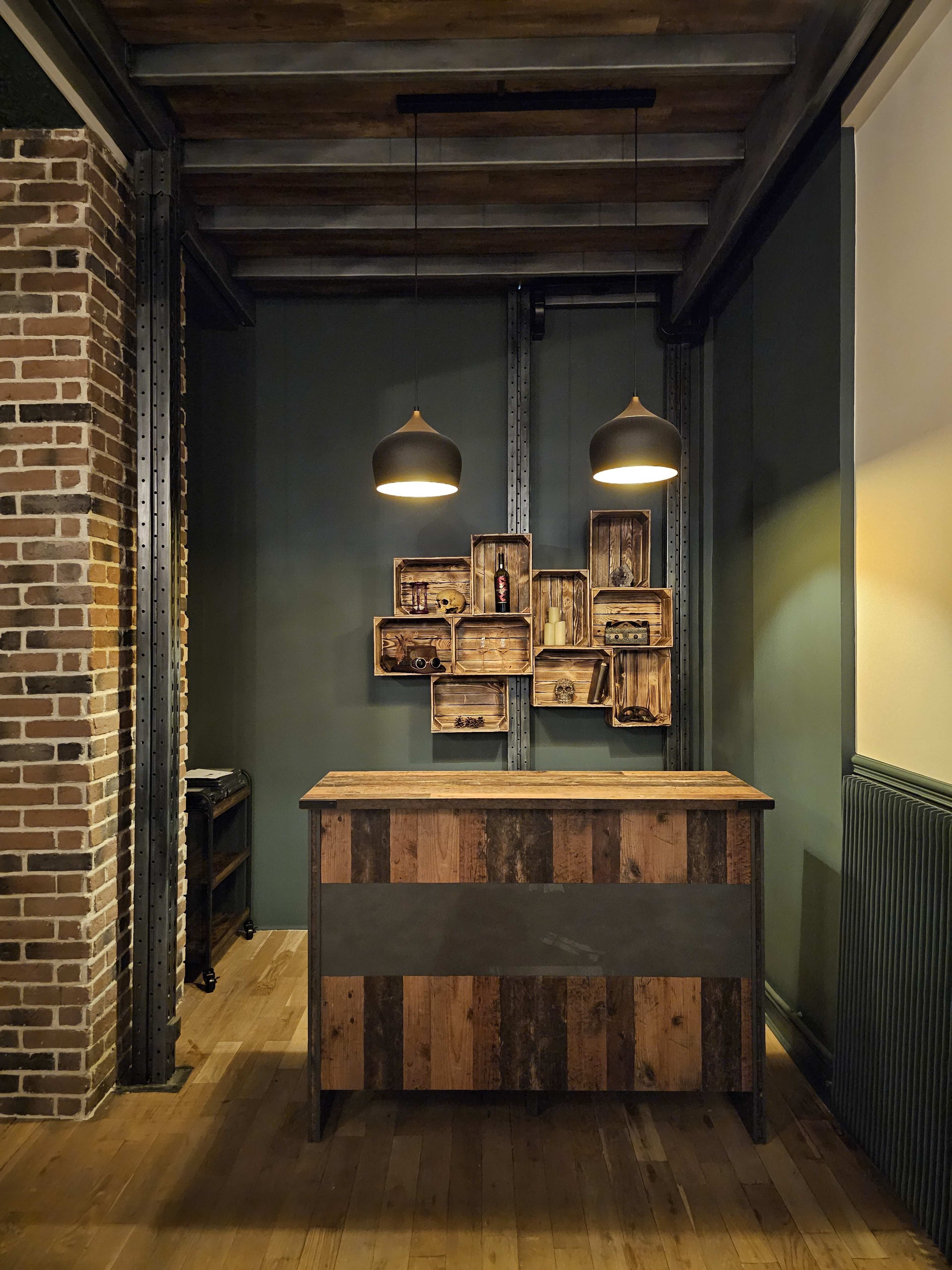 A wooden reception desk with pendant lights and wall-mounted wooden shelves against a dark green wall.