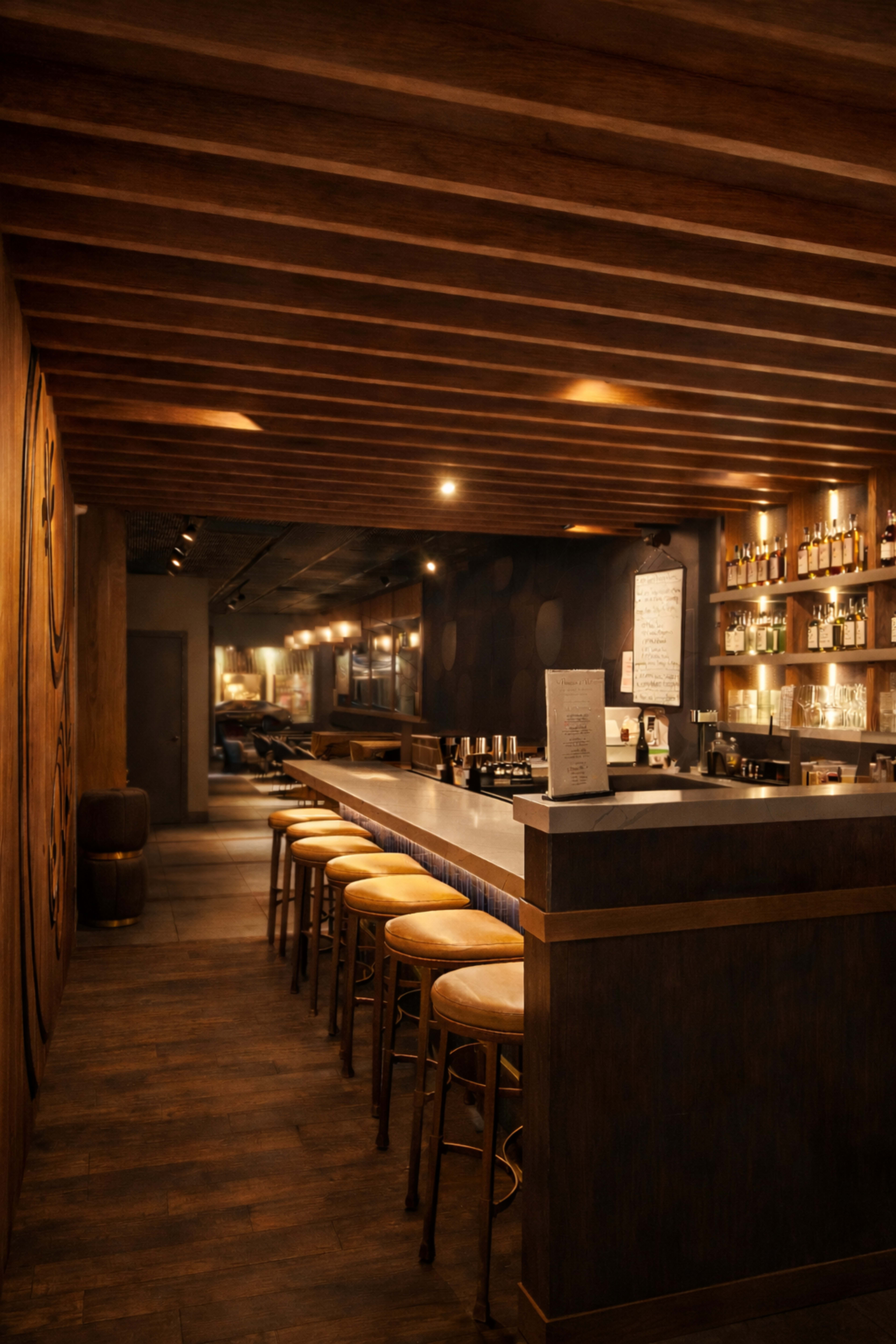 The image shows a wooden bar area with high stools, dim lighting, and shelves displaying various bottles along the back wall.