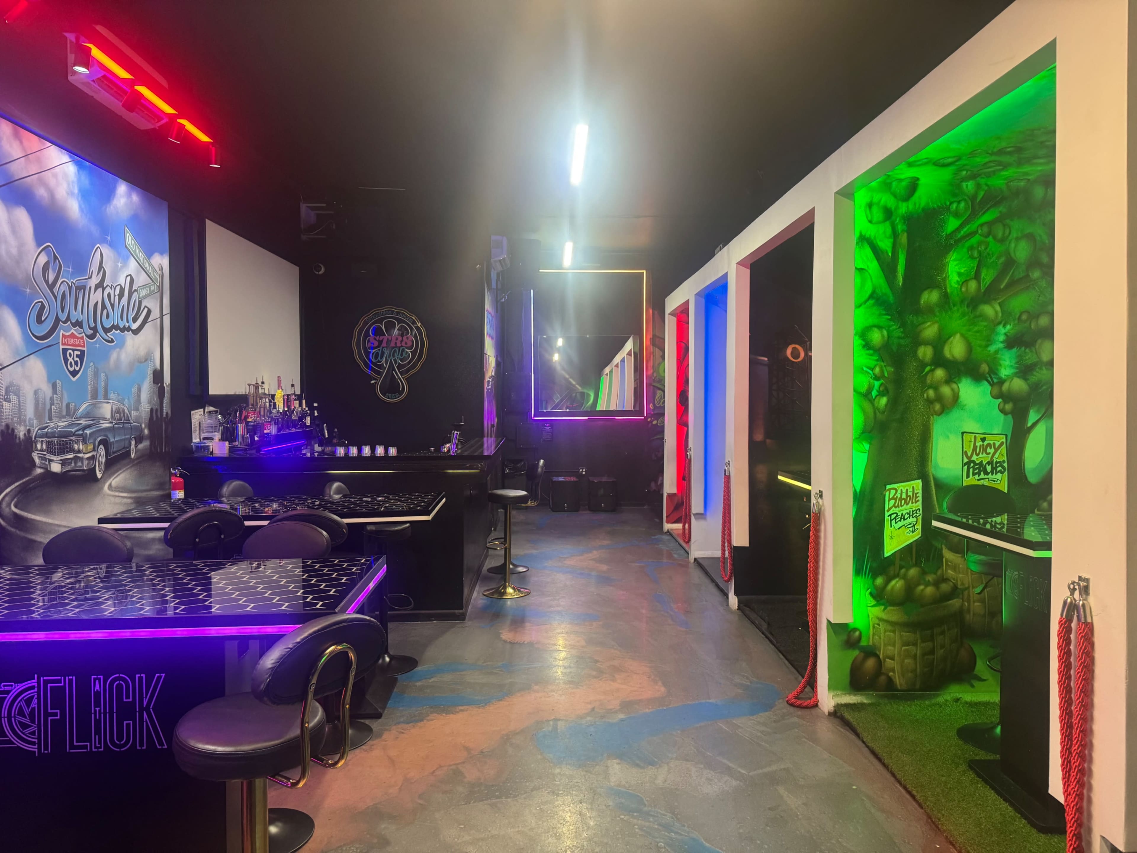The image shows a vibrant interior of an entertainment venue with colorful lighting, a bar area, and a section featuring themed wall designs.