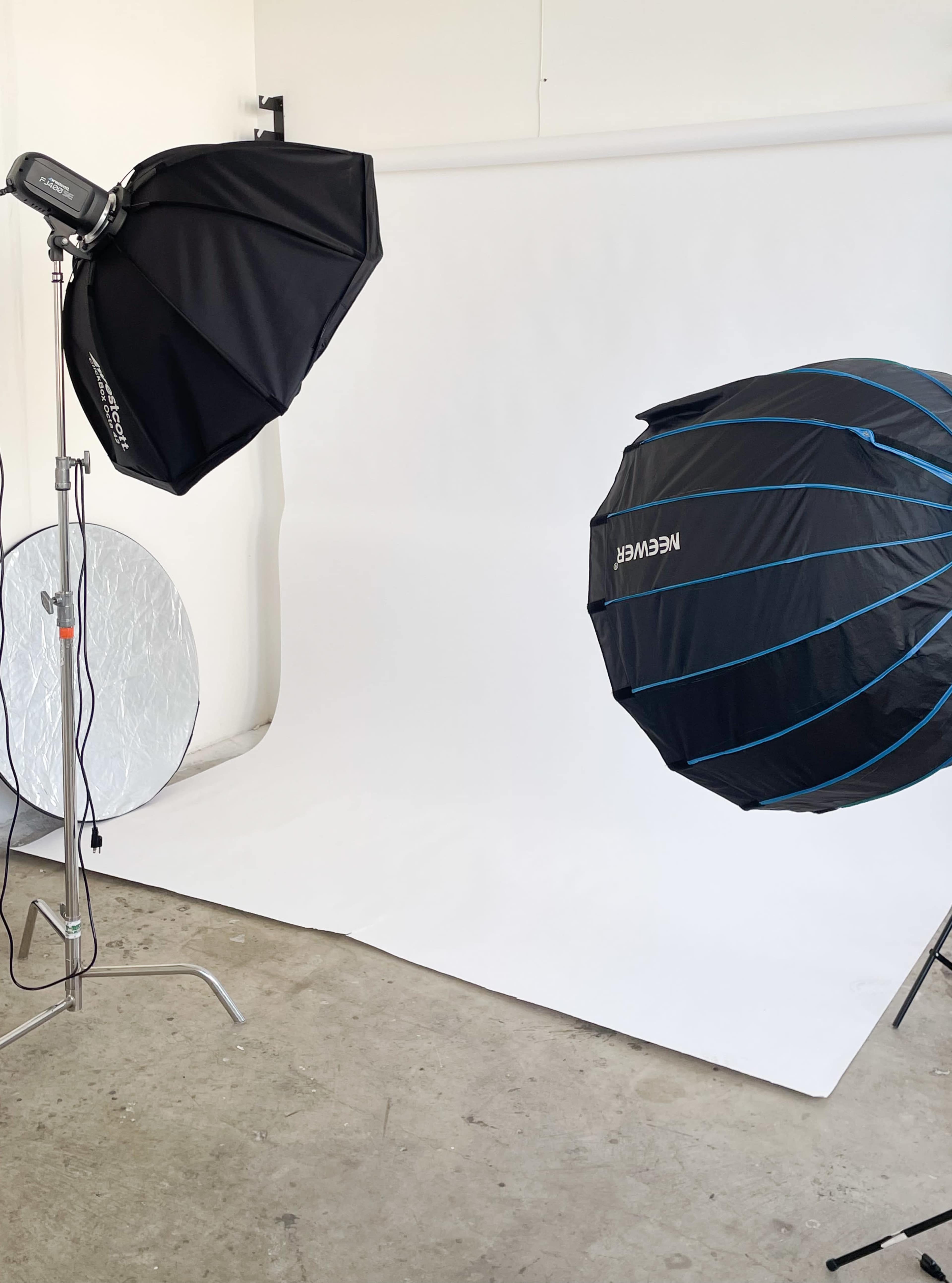 The image shows a photo studio setup featuring two light sources with softboxes and a plain white backdrop on the floor.