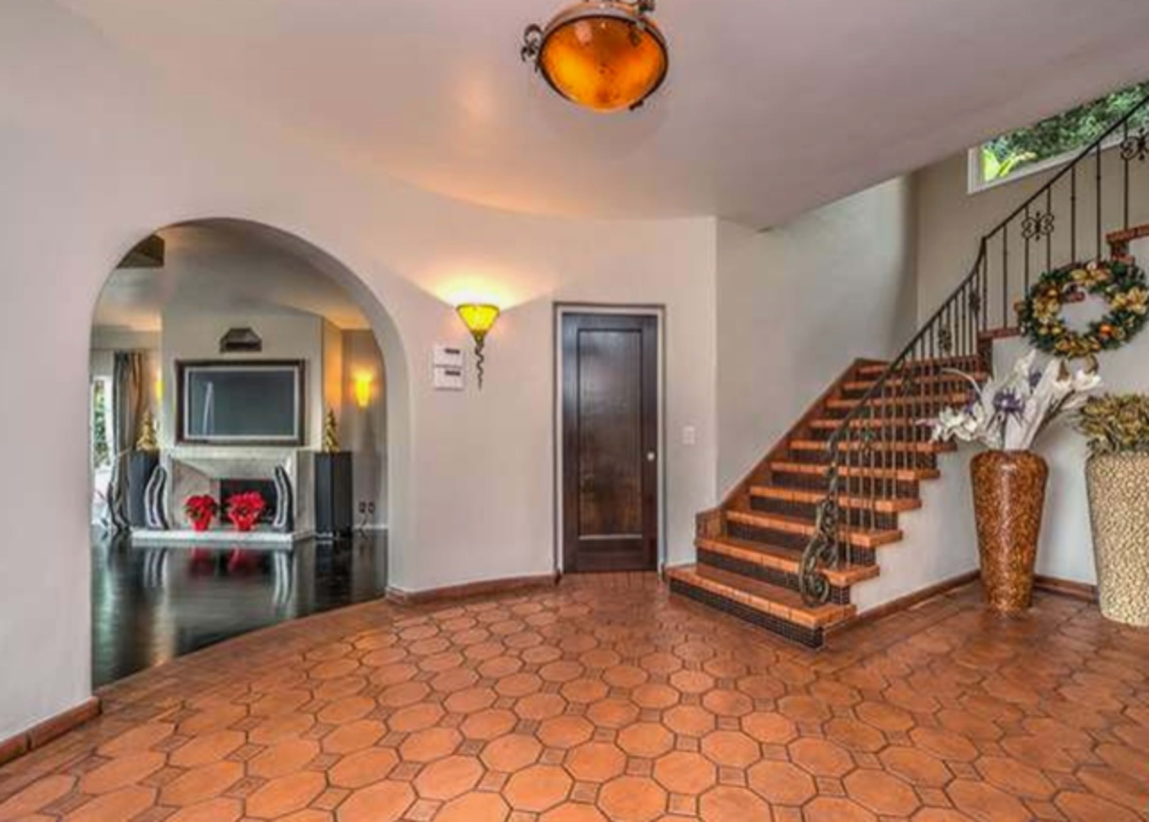 The image shows a tiled entryway with a staircase leading to an upper level, an arched entry to a living area, and decorative vases on either side.