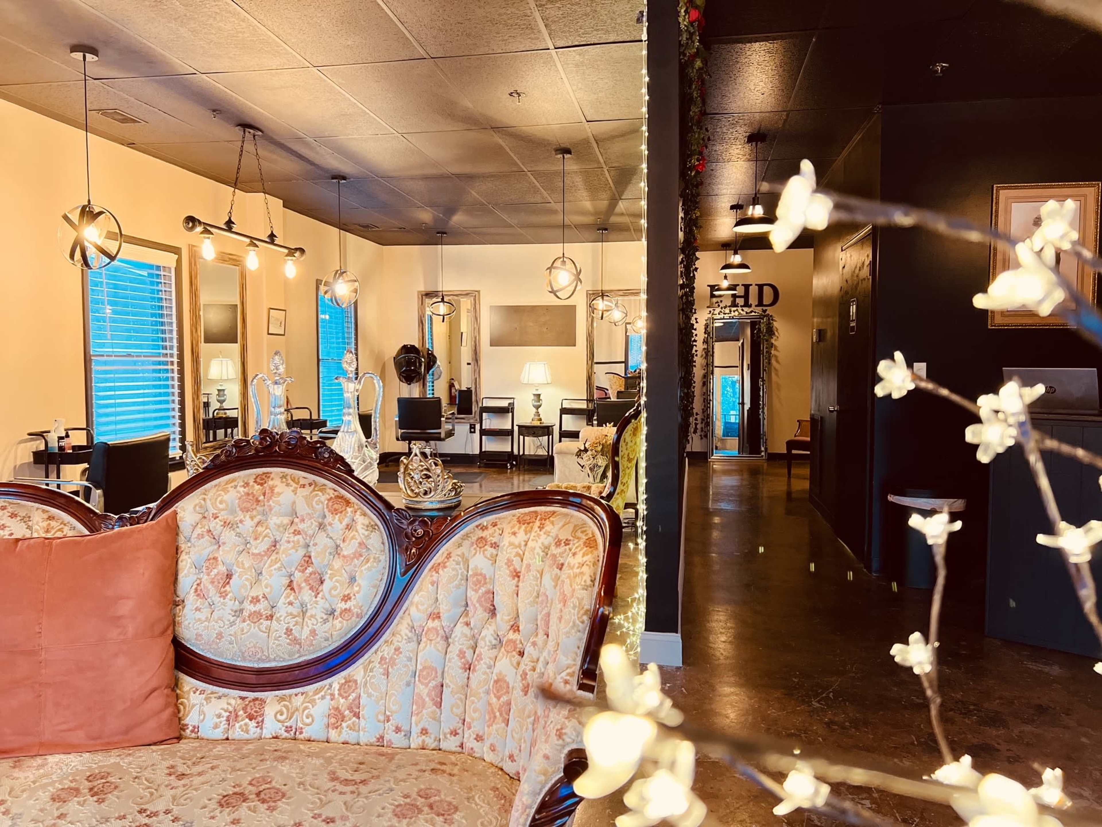 The image shows a salon interior featuring a vintage-style couch in the foreground, with salon stations and decorative lighting visible in the background.