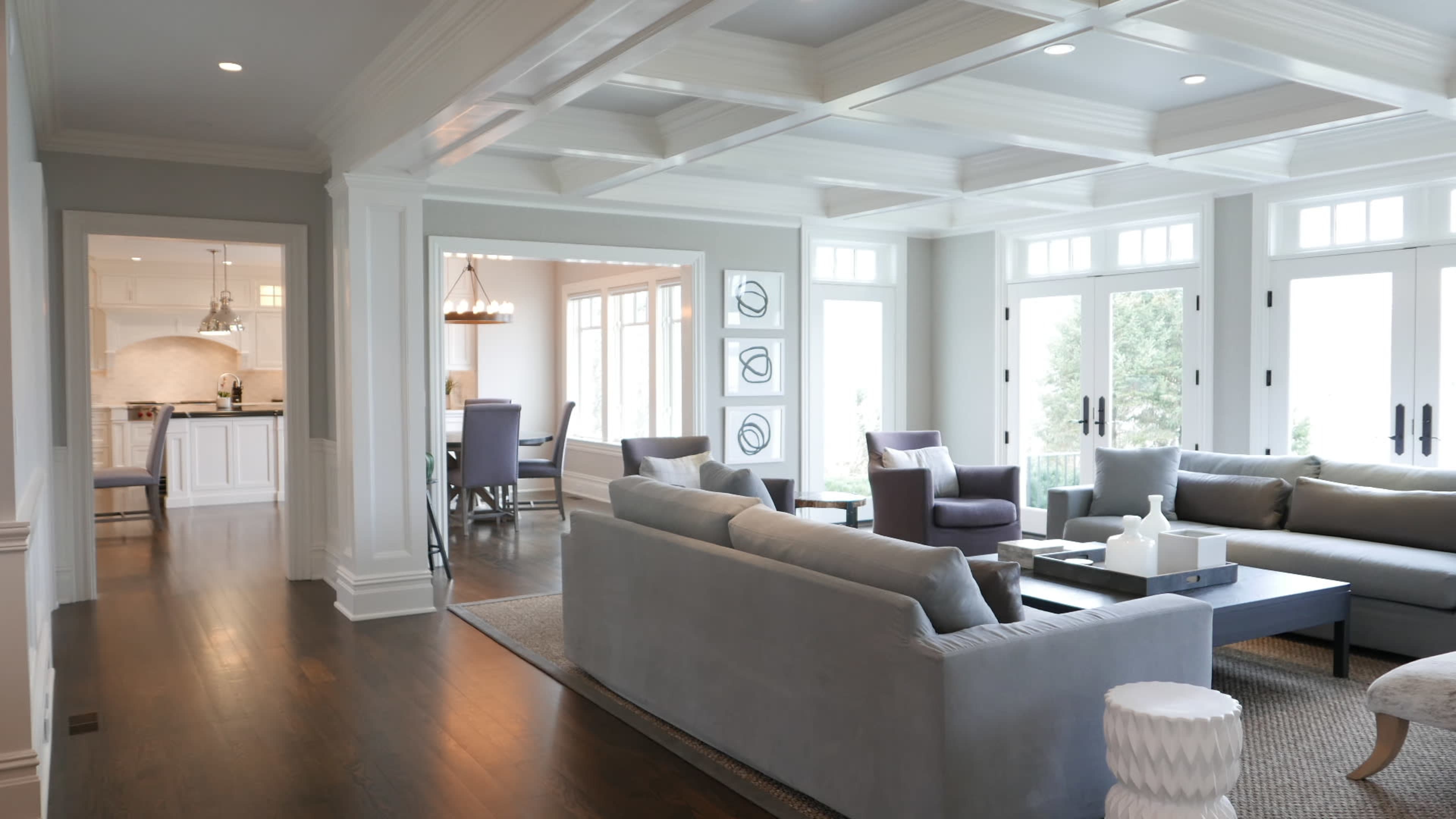 A spacious living room features a light gray sofa, a coffee table, and large windows that allow natural light to fill the space.