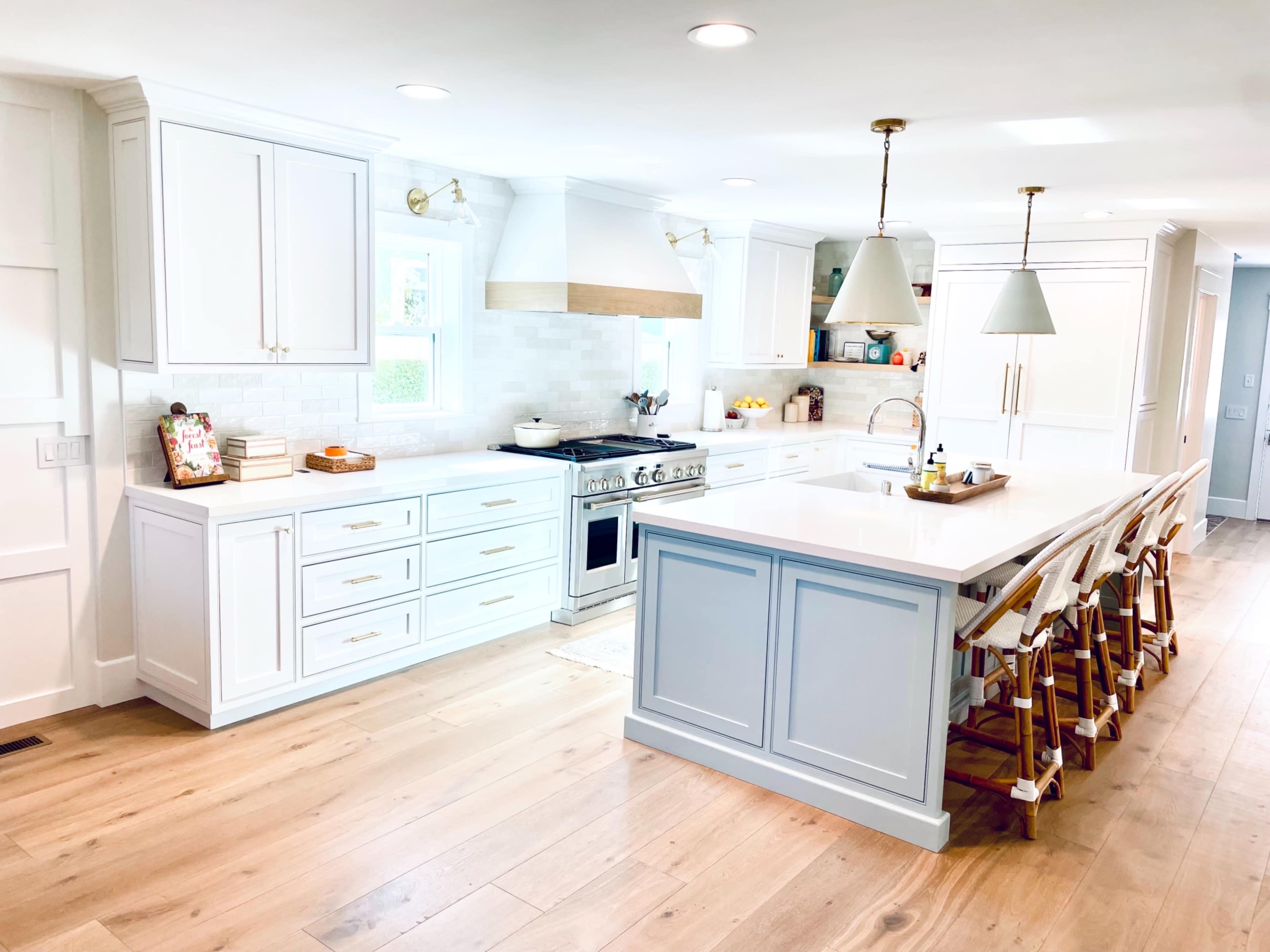 A bright, modern kitchen features white cabinetry, a large island with seating, and stainless steel appliances.