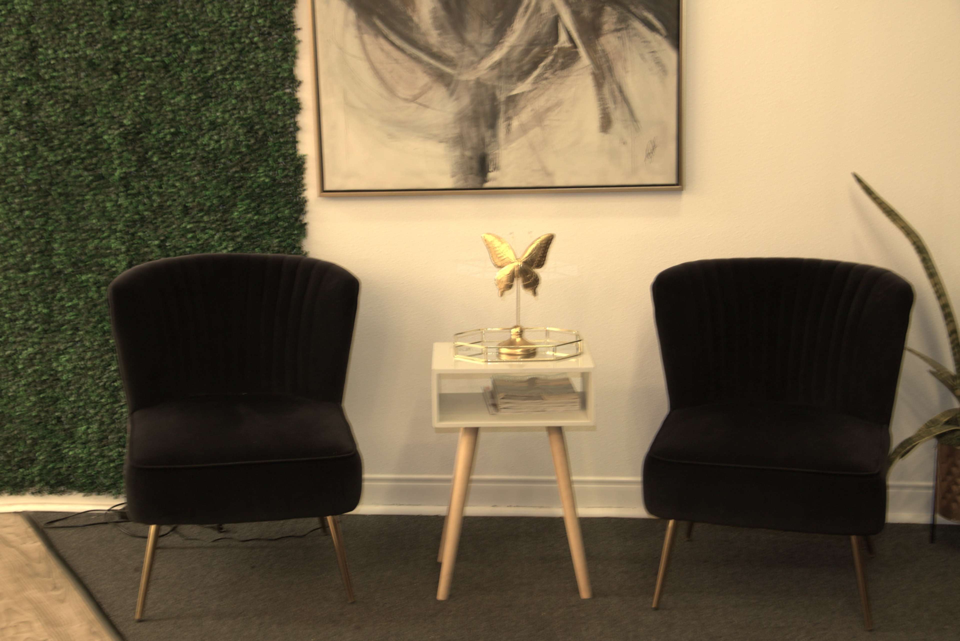 The image shows two black velvet chairs facing each other with a small table featuring a gold butterfly sculpture and a green wall in the background.