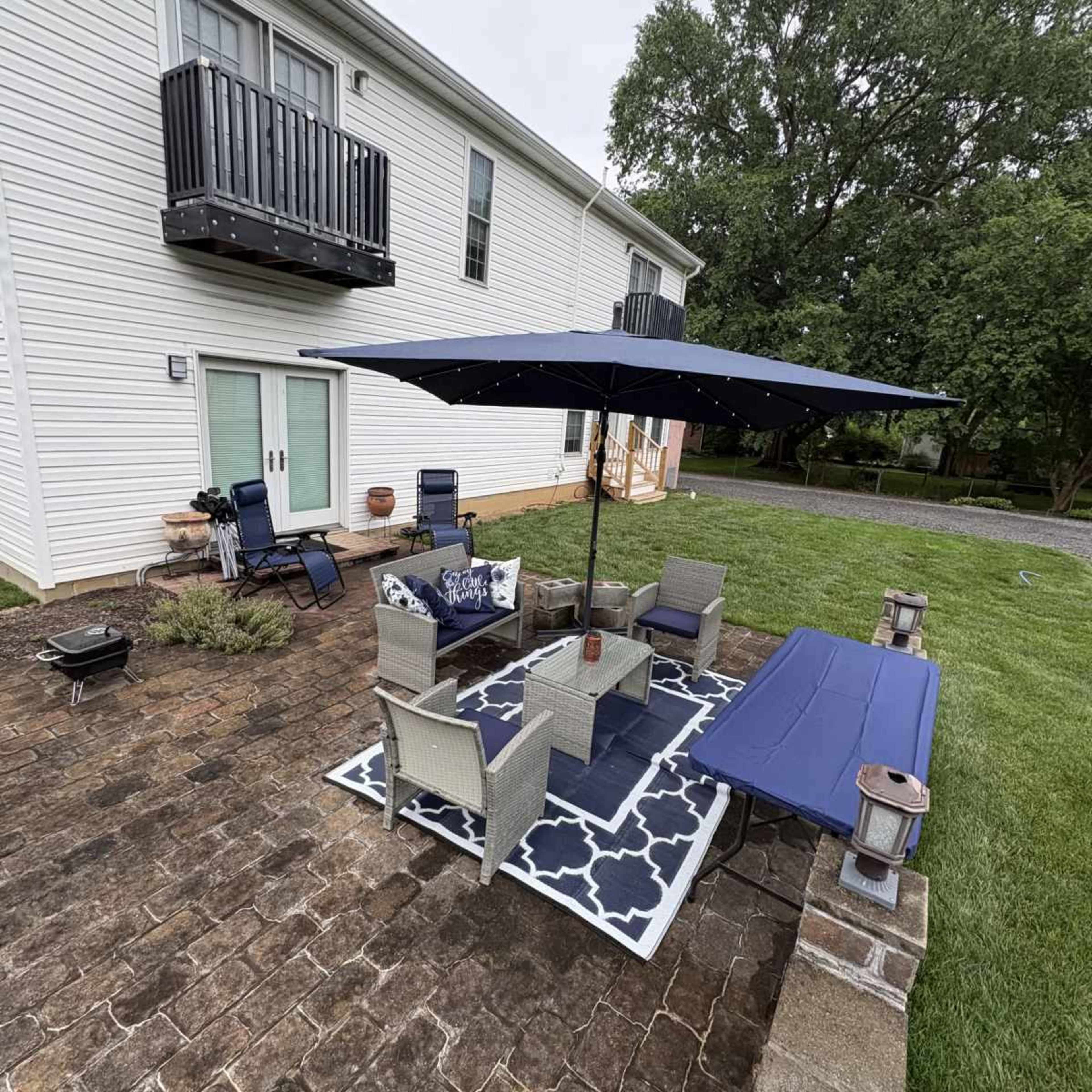 The image shows a backyard patio featuring a seating area with a large umbrella, a table, and a barbecue grill.