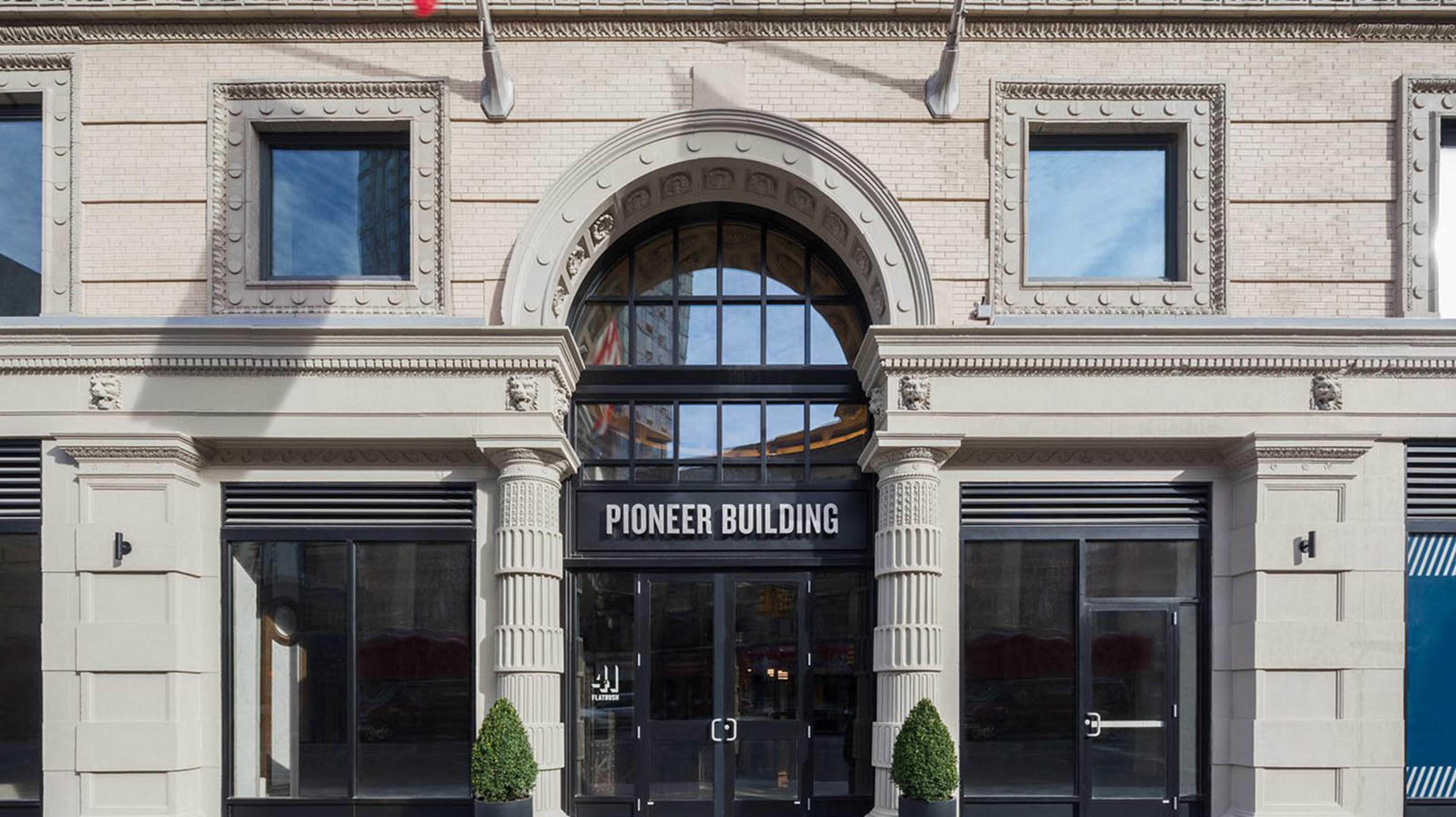 The image shows the facade of a historic building labeled "Pioneer Building," featuring decorative architectural details and large glass doors.