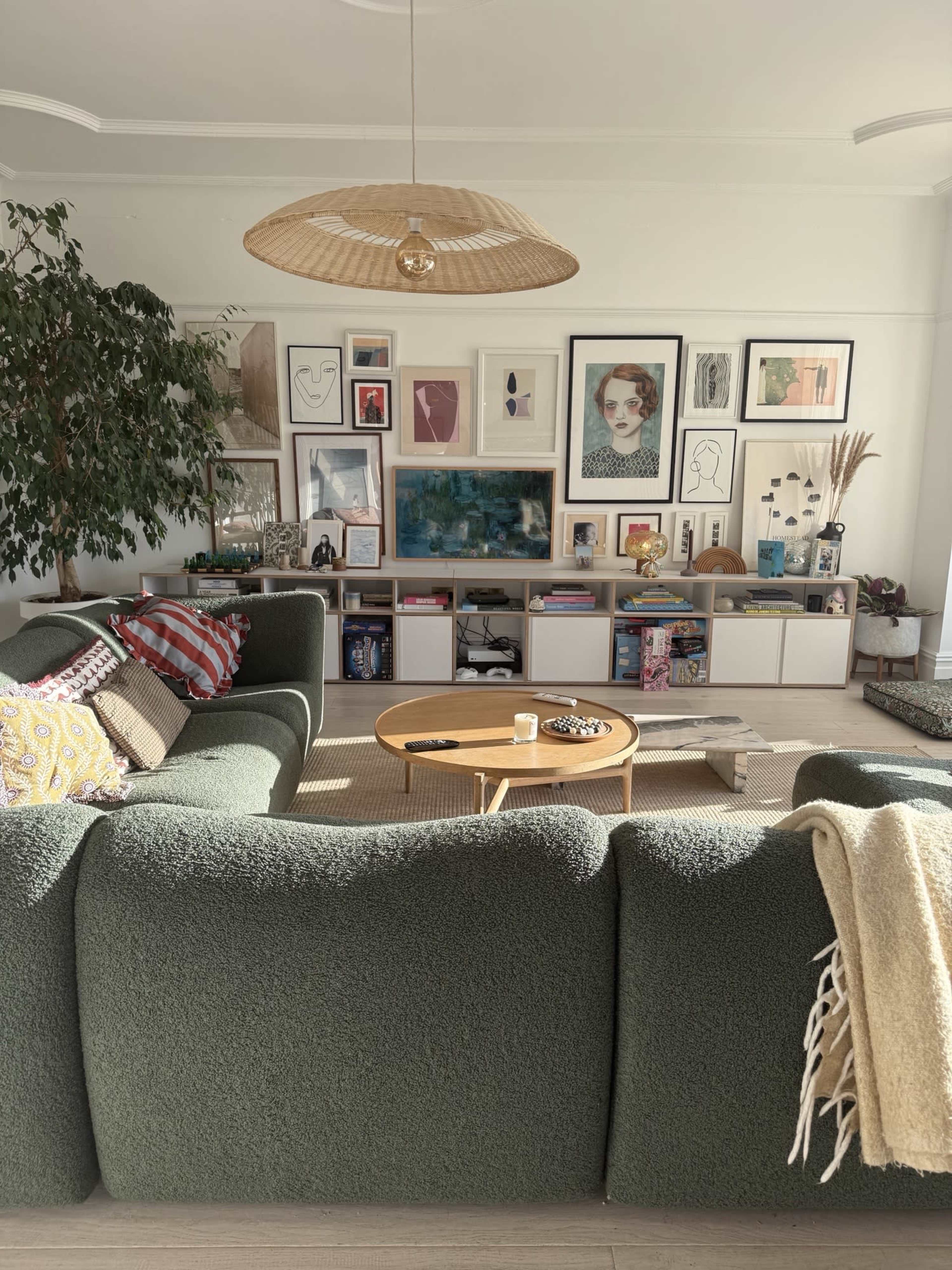 The living room features a large green sectional sofa facing a gallery wall adorned with various framed artworks and photographs, while a round coffee table sits in front on a woven rug.