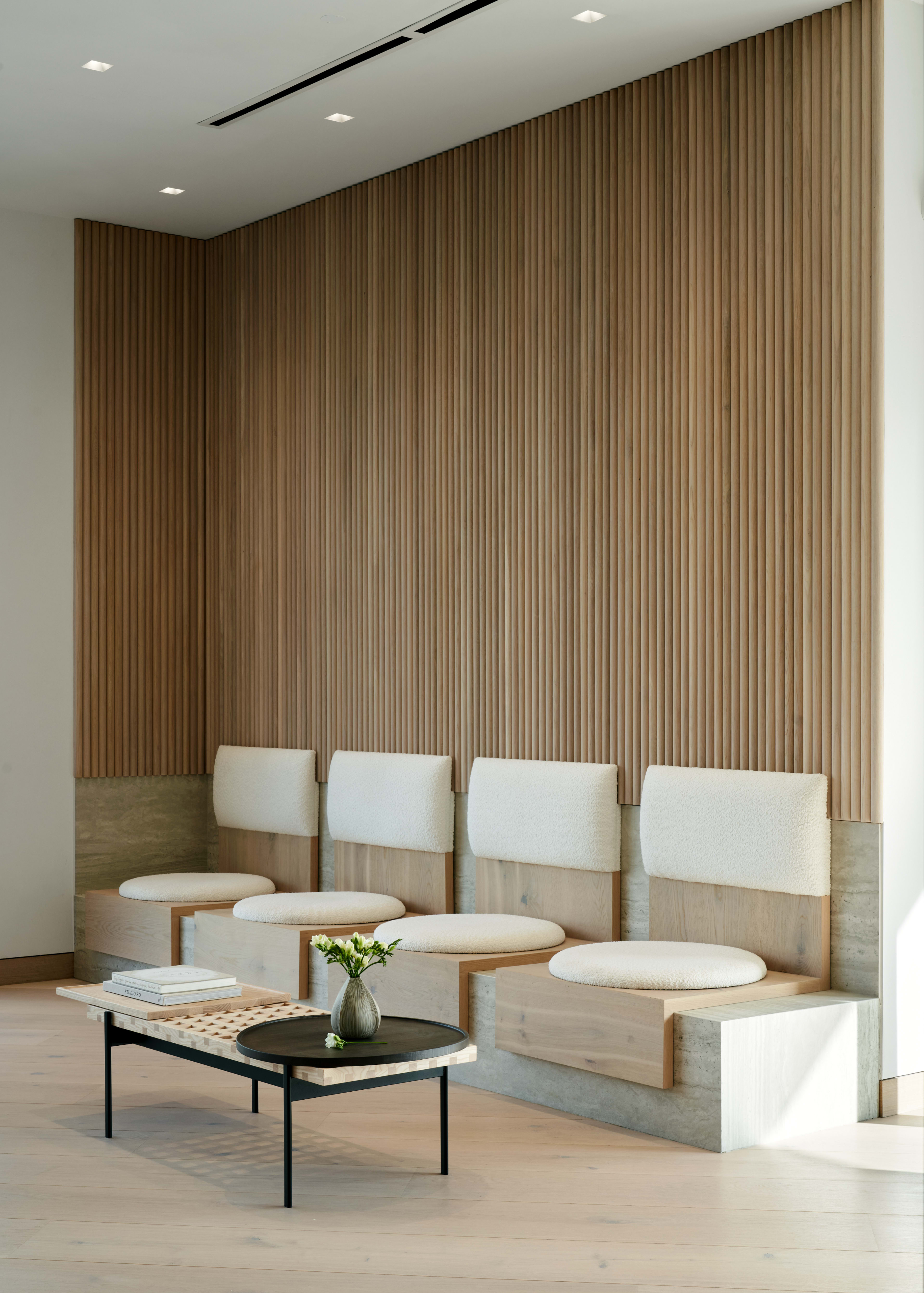 A modern seating area features a light-colored wooden wall with vertical slats, complemented by a low coffee table and cushioned bench seating.