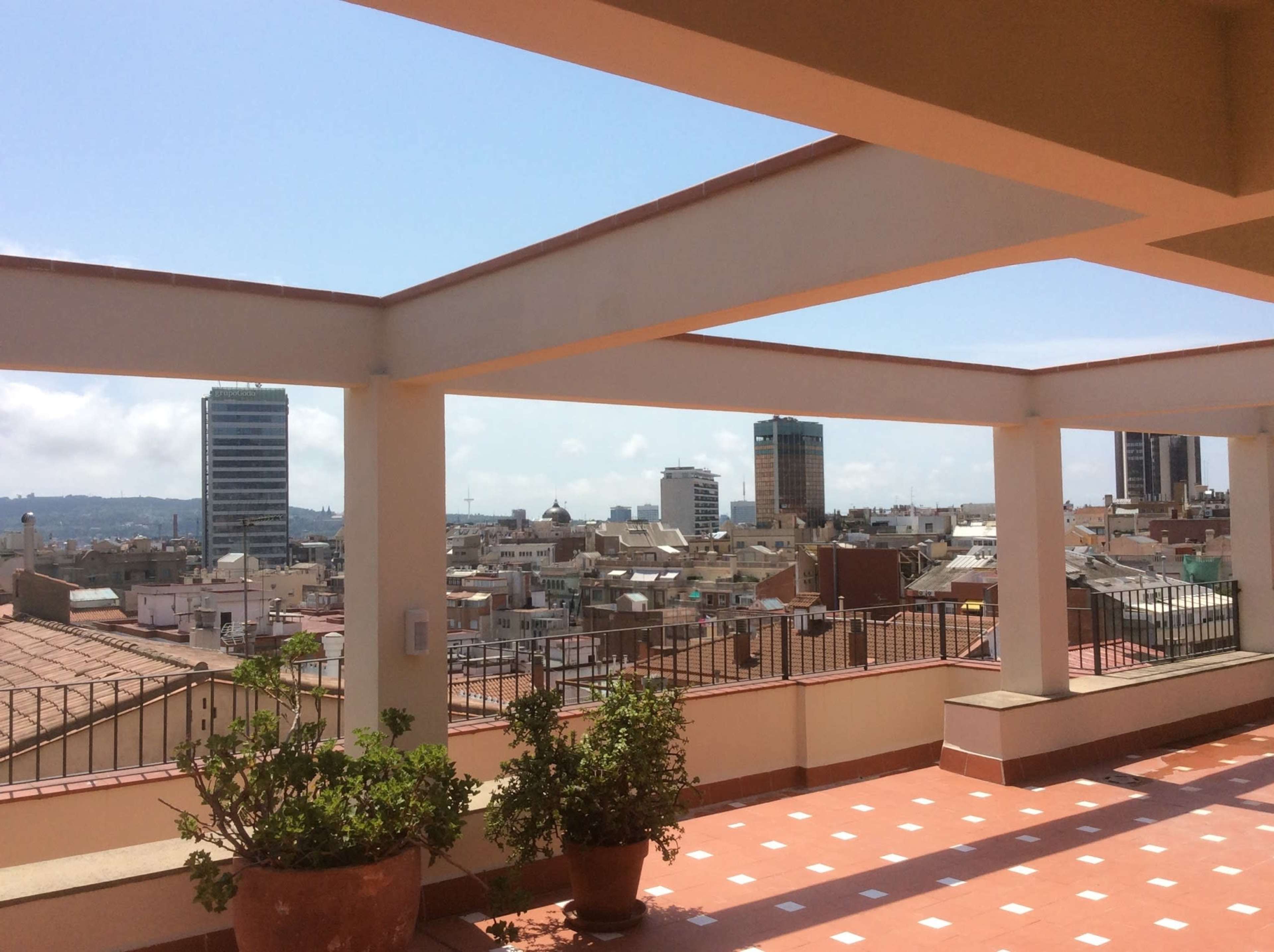 A rooftop terrace with a view of a city skyline featuring several high-rise buildings and a clear sky.