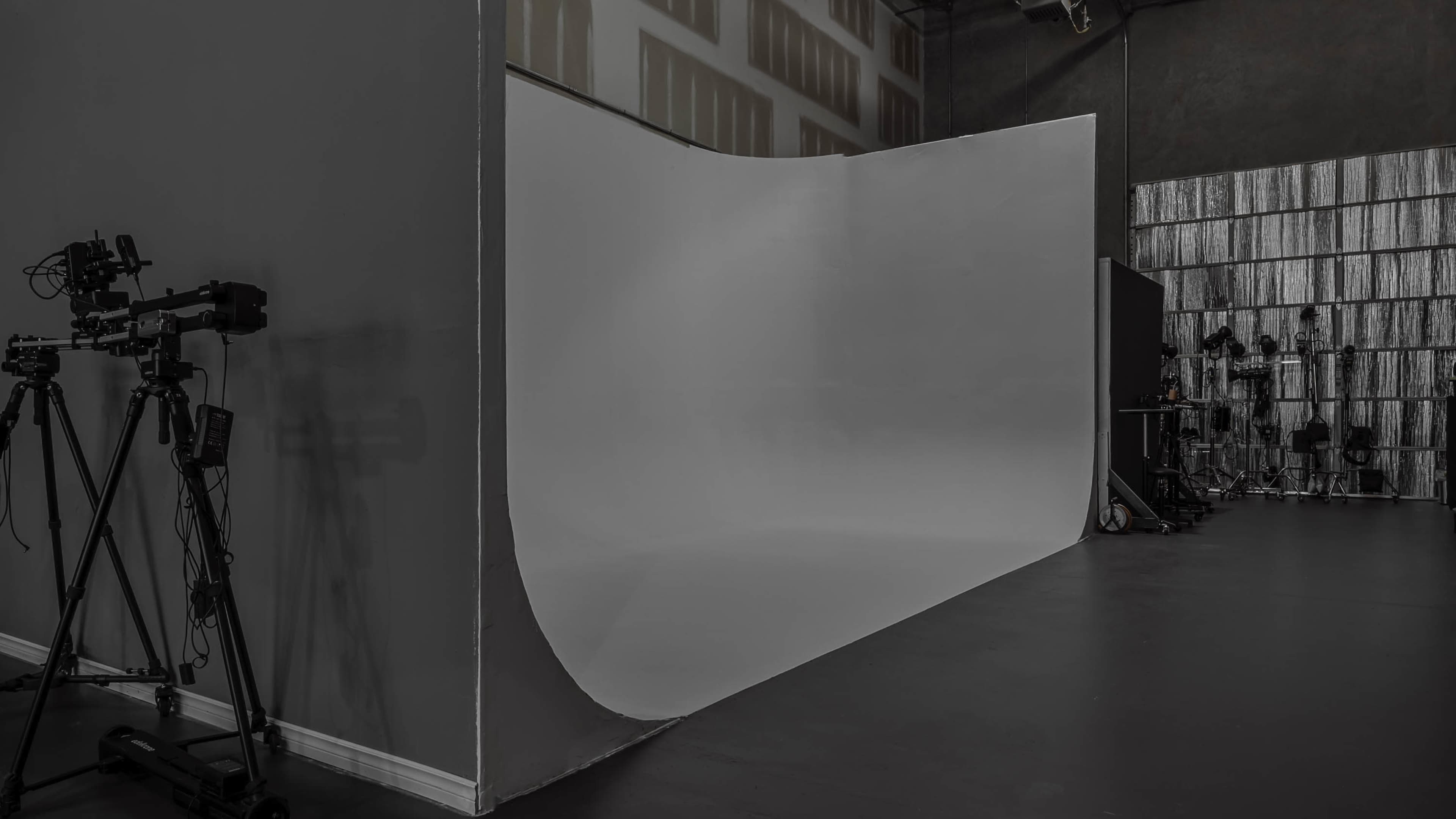 The image shows a photography studio with a large white backdrop and various photography equipment positioned to the side.
