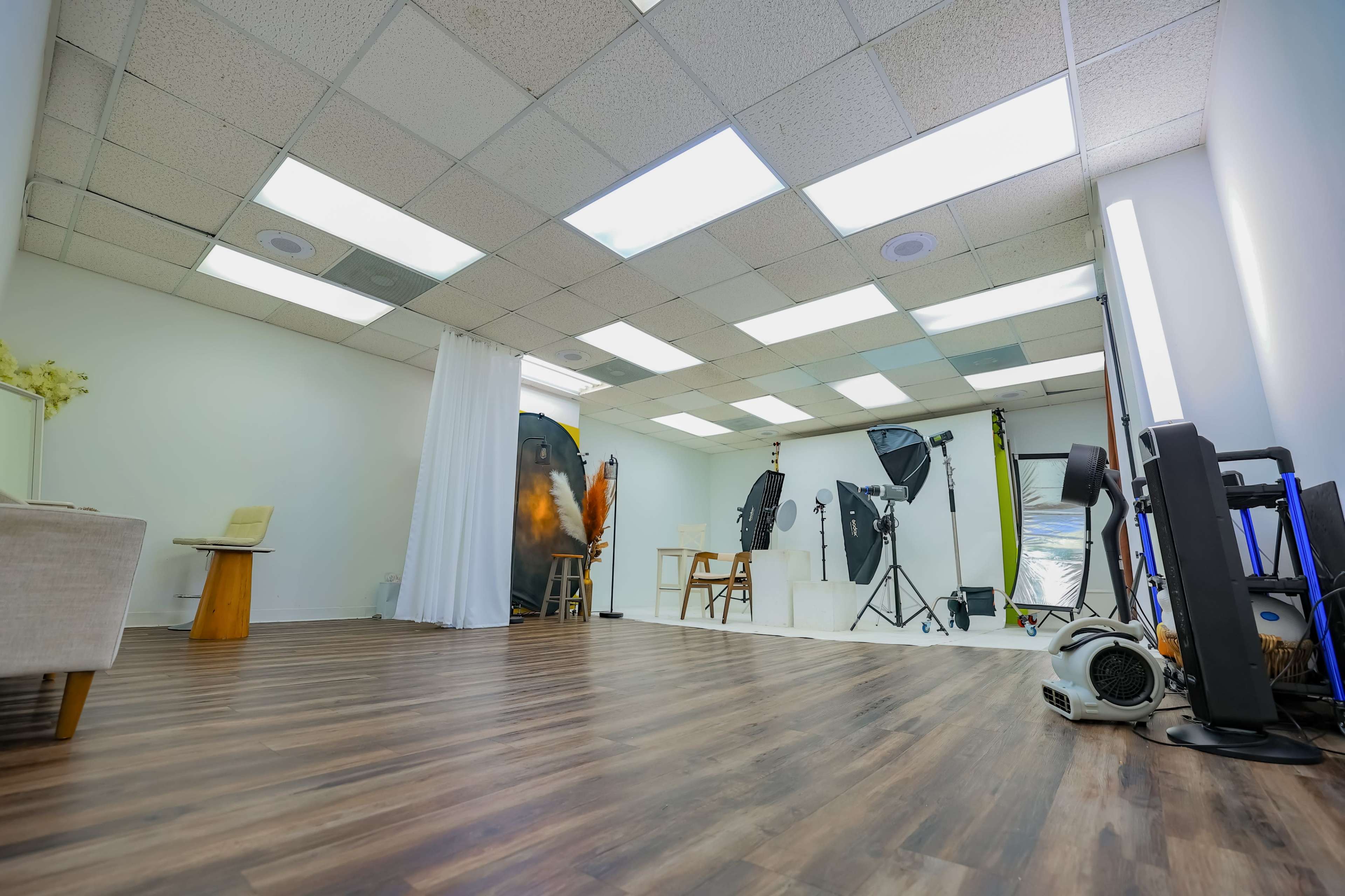 The image shows a photography studio with various lighting equipment, backdrops, and props arranged in an open space with wooden flooring.