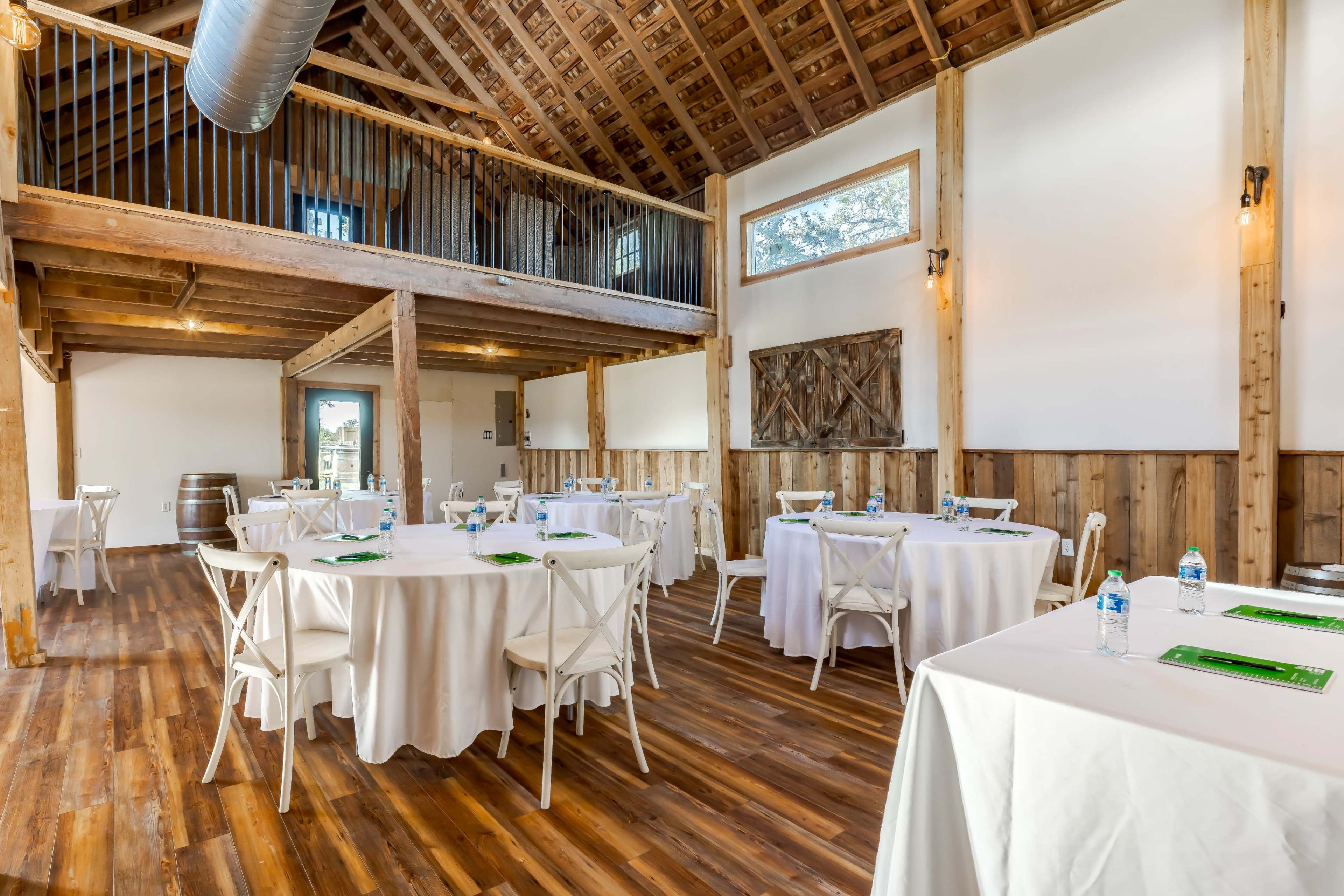 A spacious, well-lit dining area with white tablecloths and wooden accents, featuring large windows and a rustic wooden ceiling.