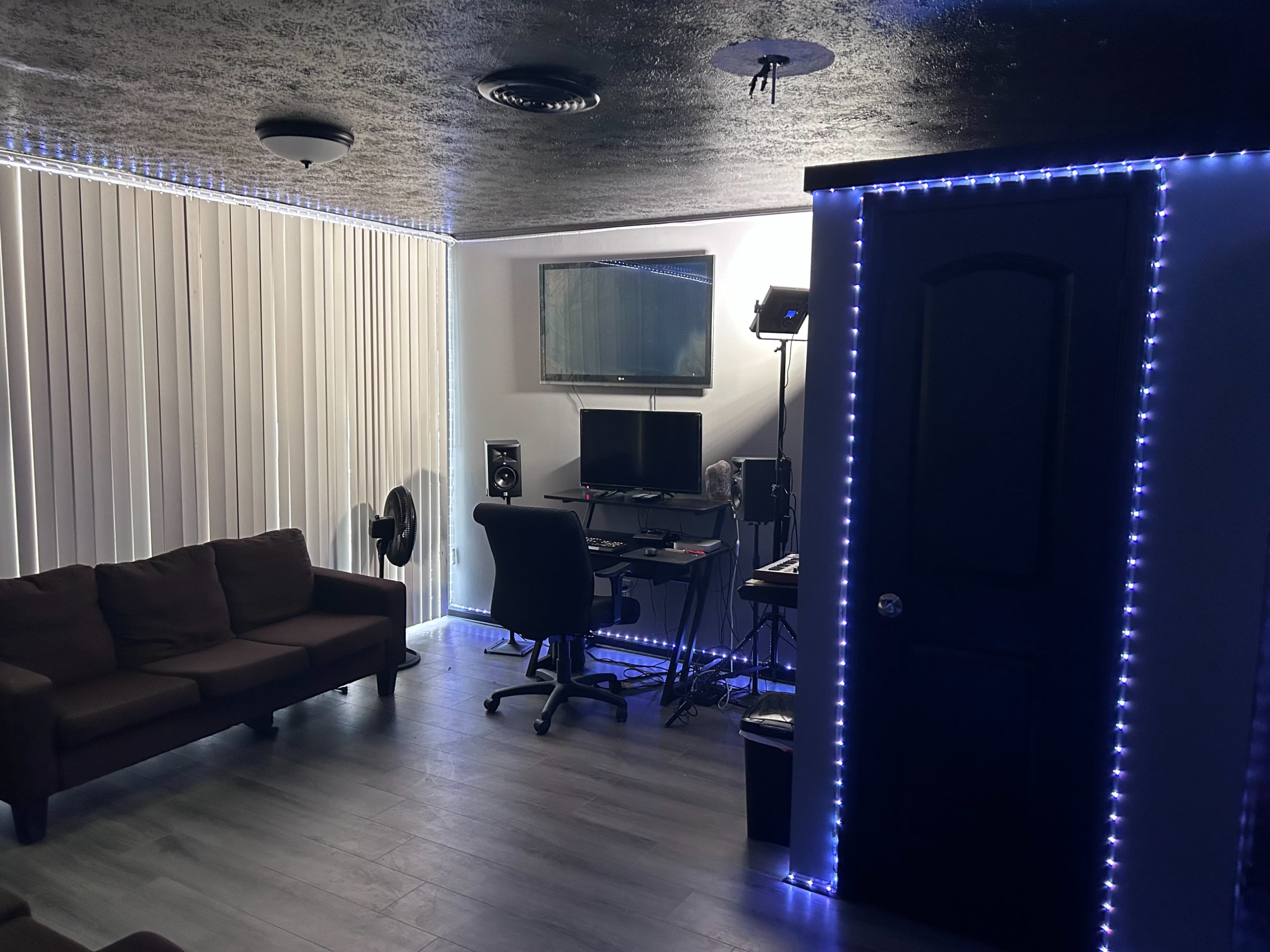 A dimly lit room featuring a sofa, a desk with computer equipment, and ambient LED lighting along the walls.