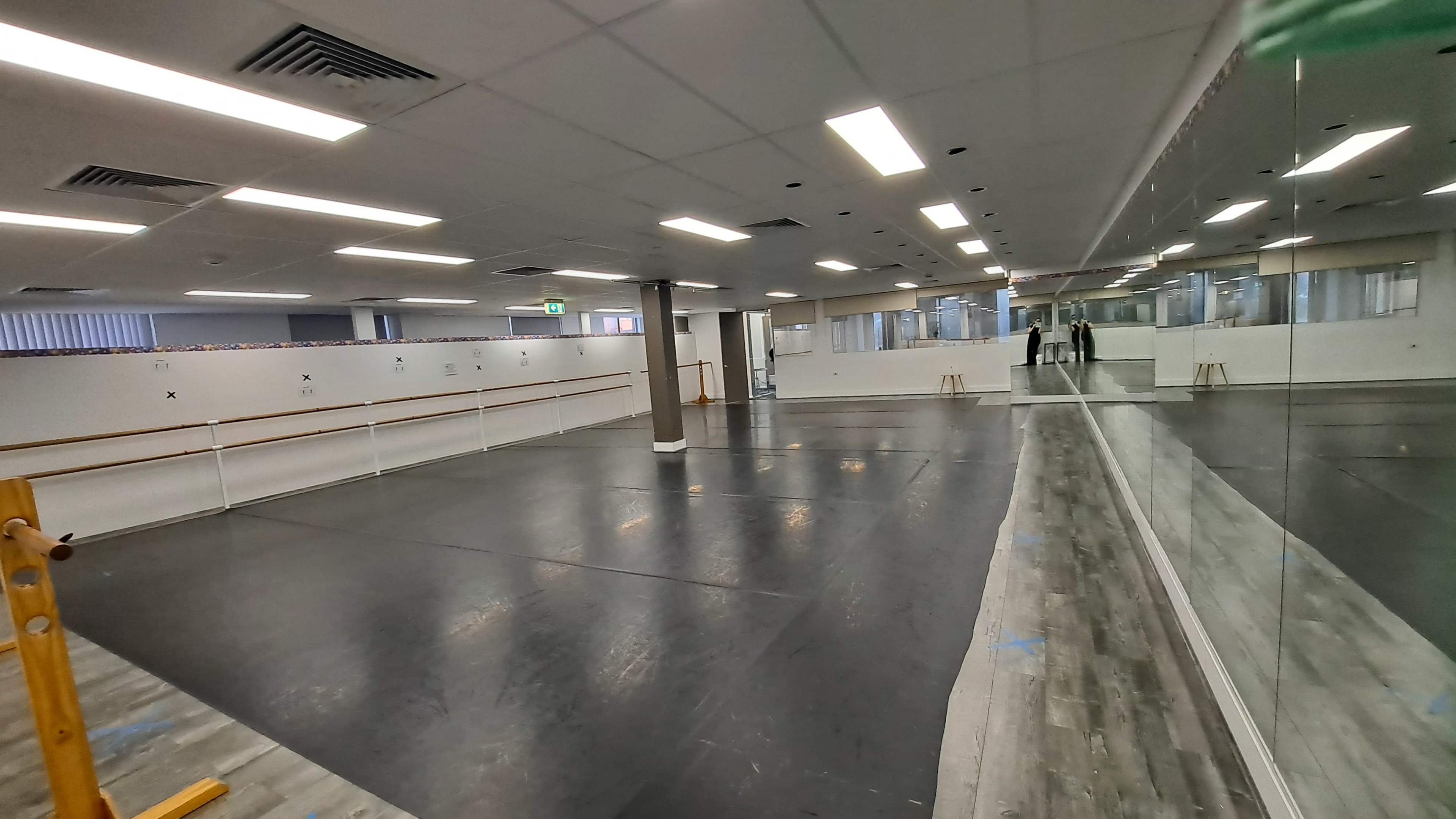 A spacious dance studio with a mirrored wall, ballet barre, and smooth black flooring.
