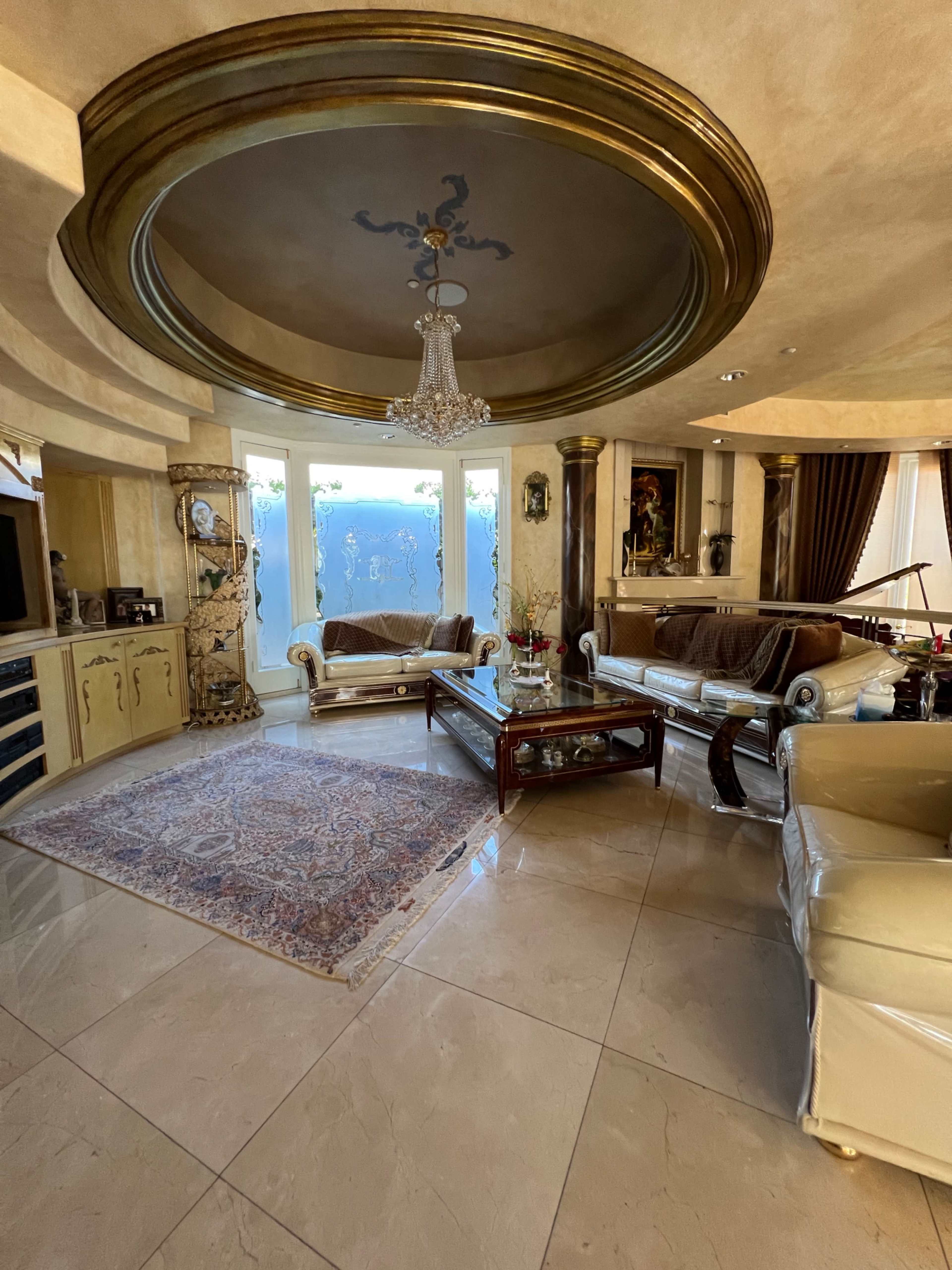A luxurious living room with a circular ceiling, a chandelier, elegant furniture, and large windows.