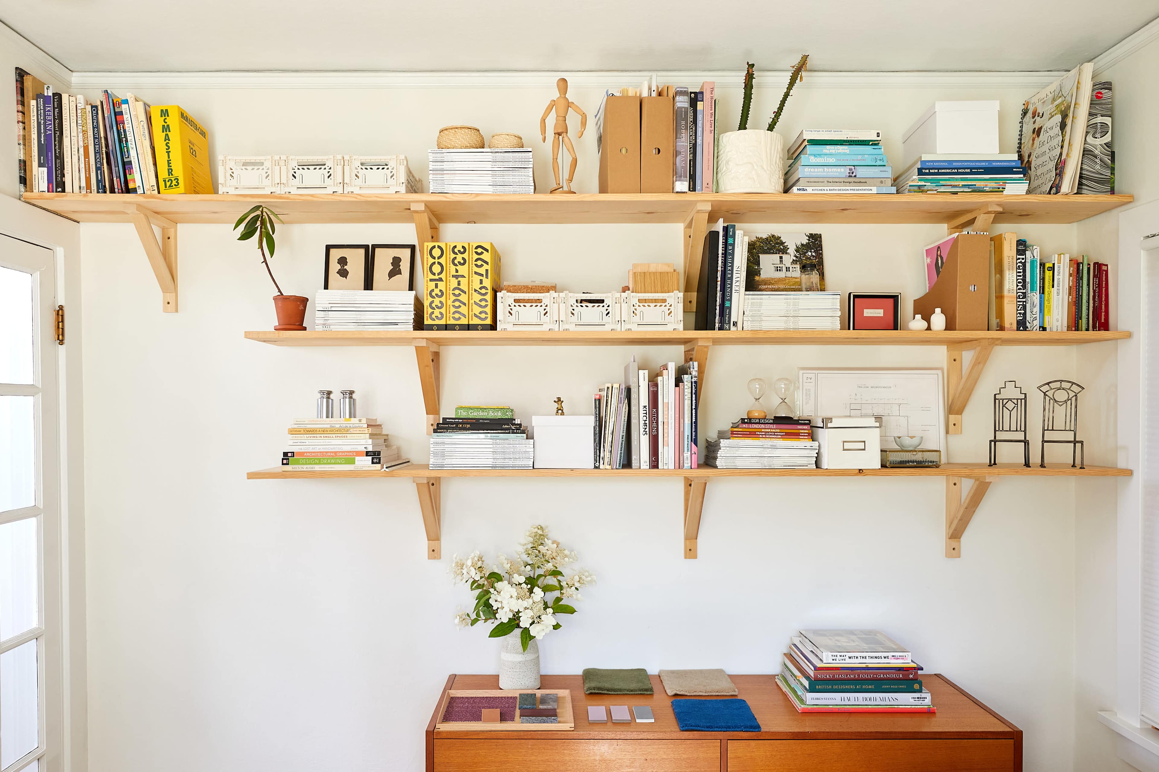 A wooden shelf unit filled with books, decorative items, and a small potted plant against a light-colored wall.