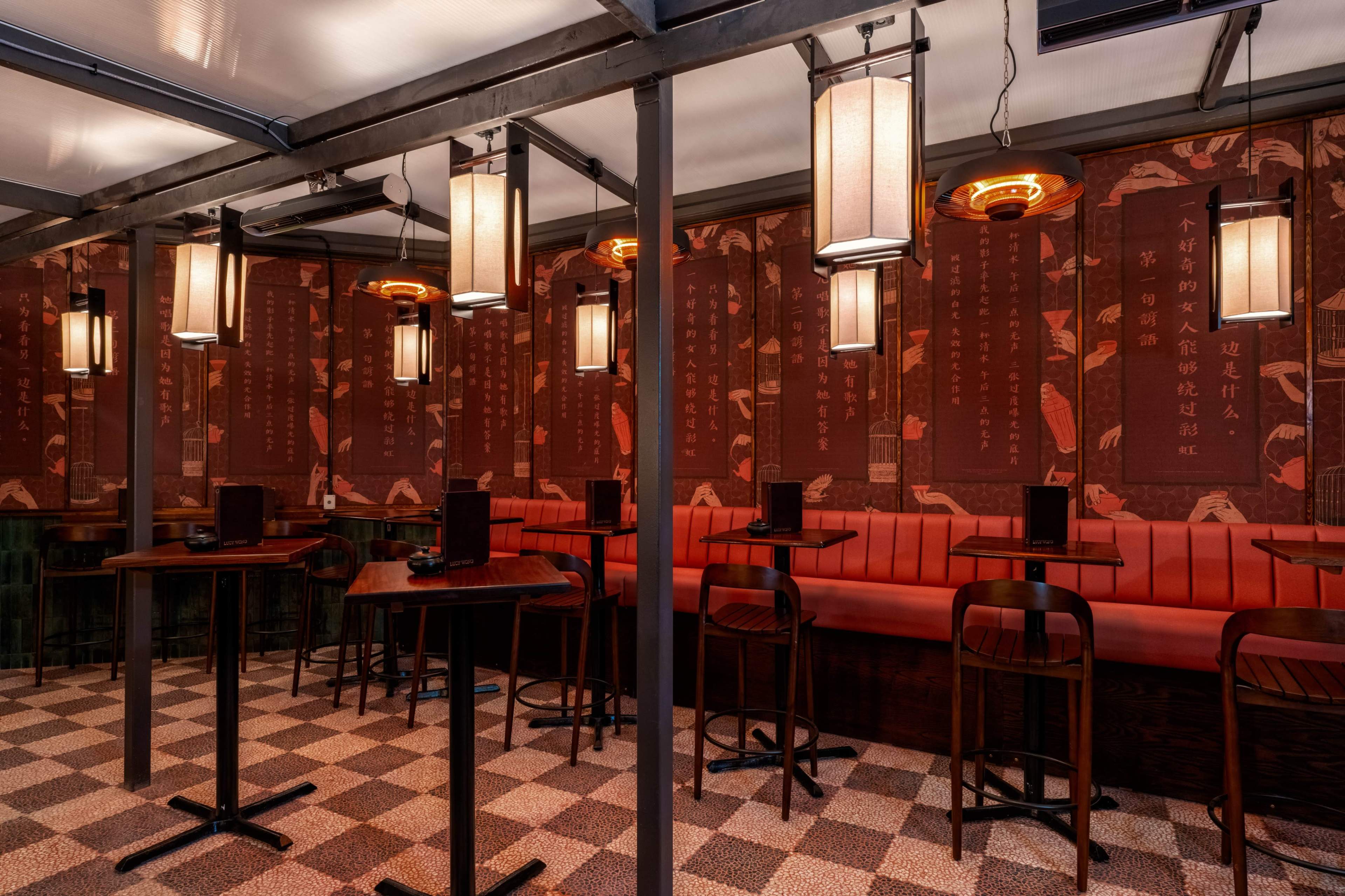 The image shows an indoor restaurant with dark wooden furniture, ambient lighting from hanging lamps, and walls adorned with patterned red wallpaper featuring Chinese characters.