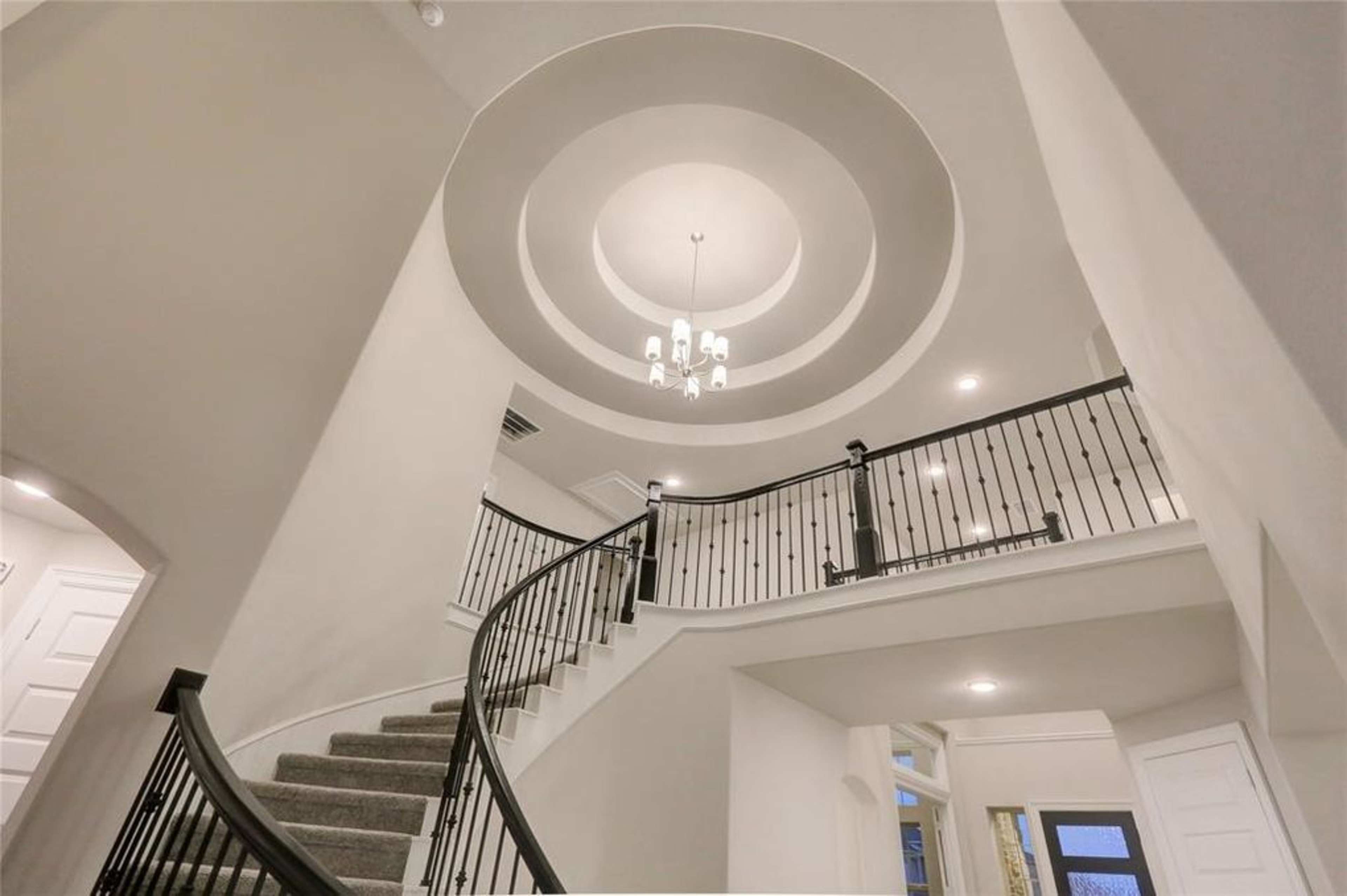 A spiral staircase leading to a ceiling with a circular design and a chandelier hanging in the center.