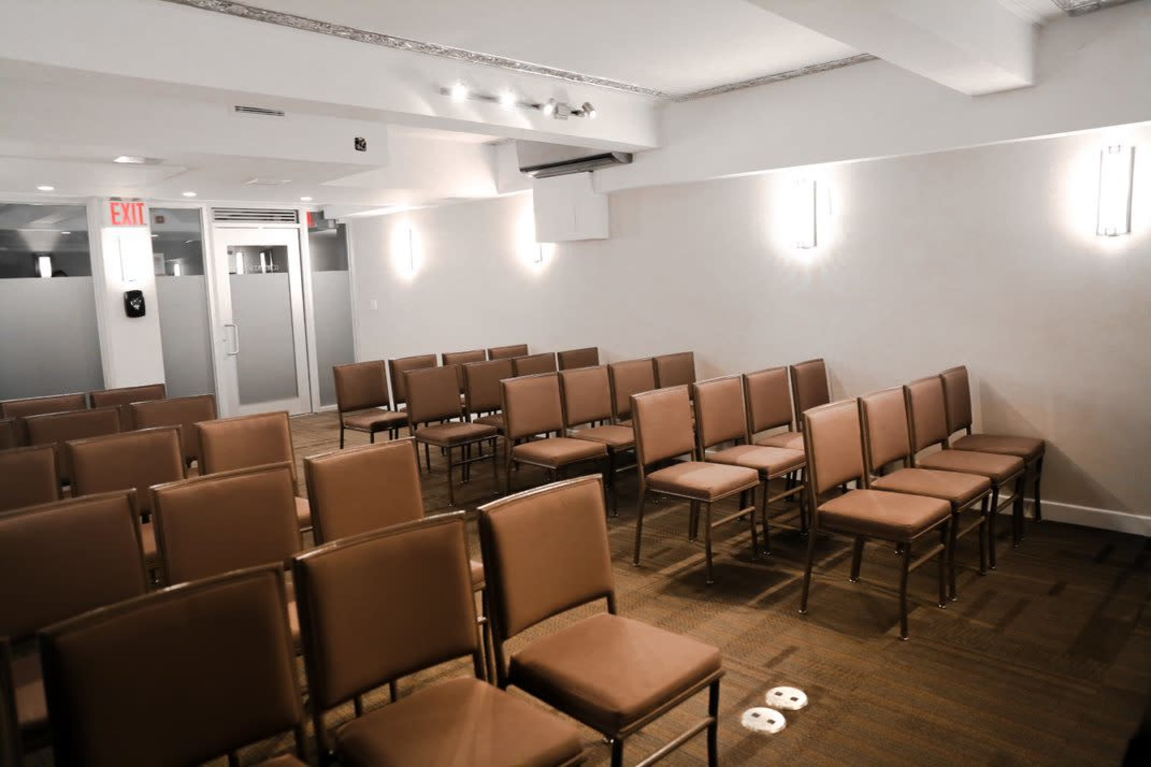 A conference room with neatly arranged rows of brown chairs facing a blank wall.