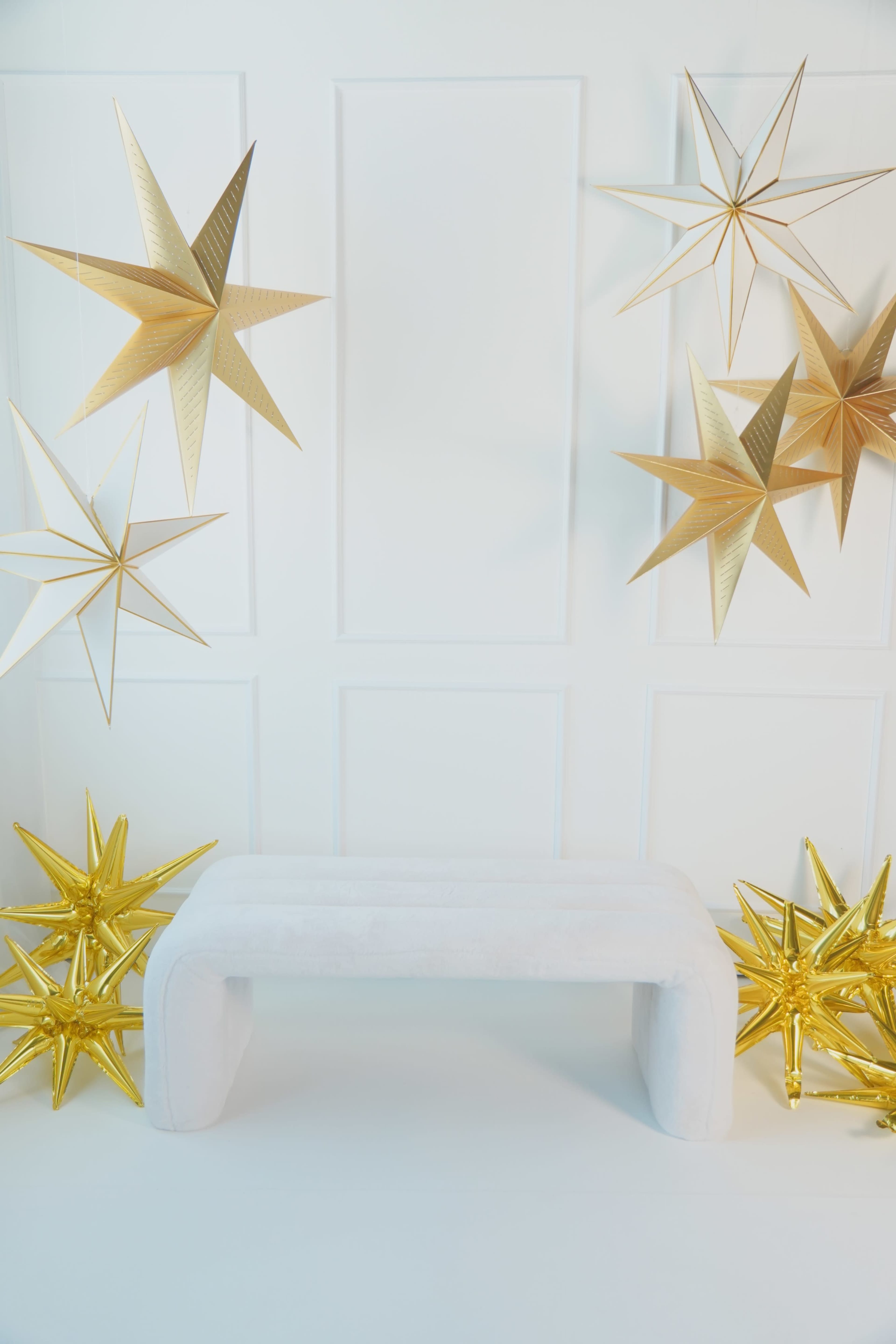 A white bench is centered in front of a white wall adorned with large gold star decorations hanging above and positioned on each side.