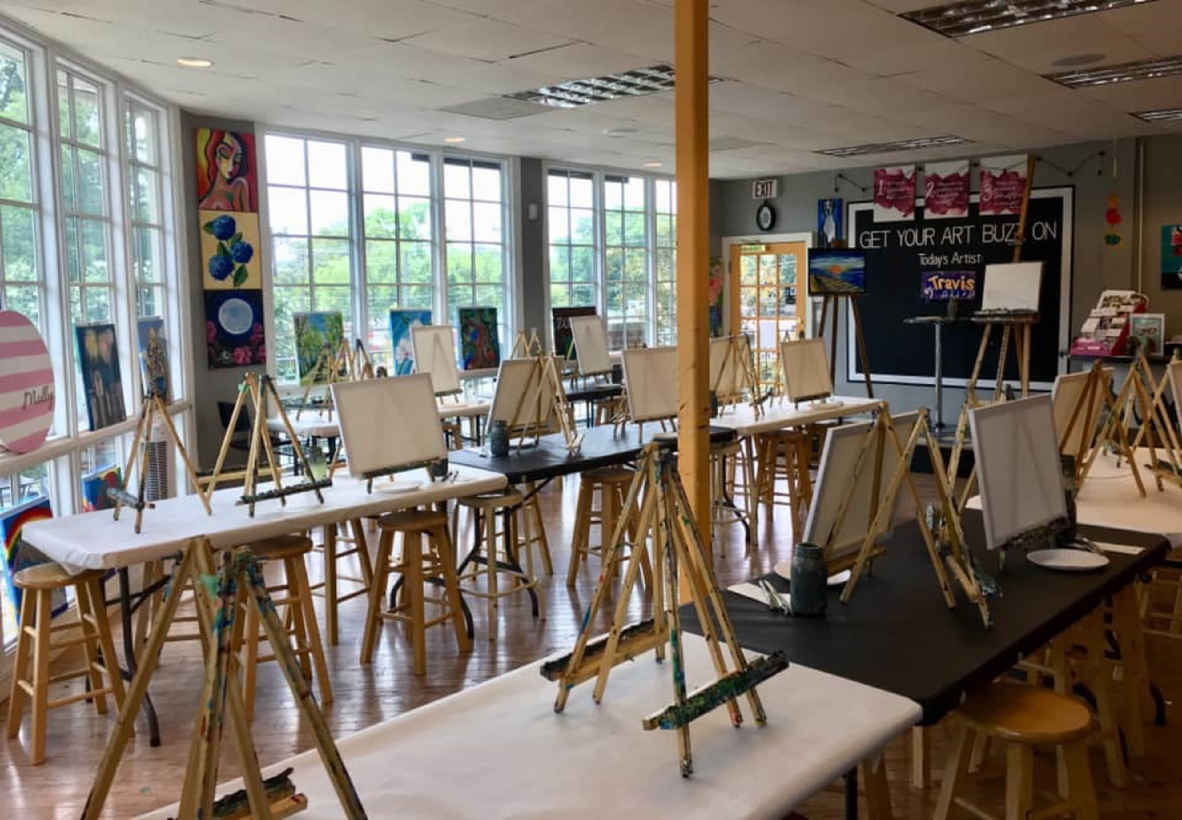 A spacious art studio is set up with multiple easels and stools arranged around the room, ready for a painting class.