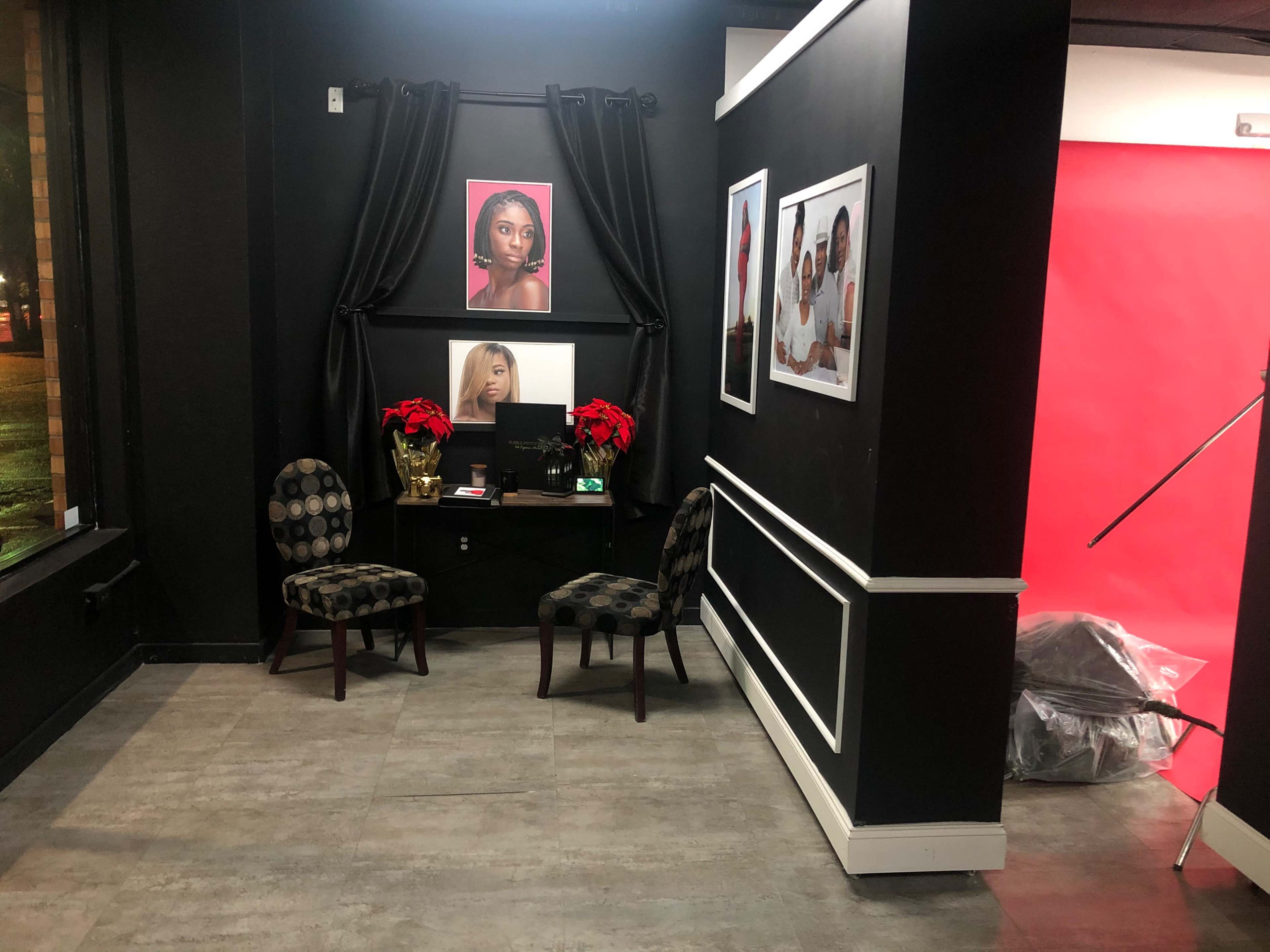 A small studio corner with two patterned chairs, a table adorned with holiday decorations, and framed portraits on the wall, backed by a red backdrop.