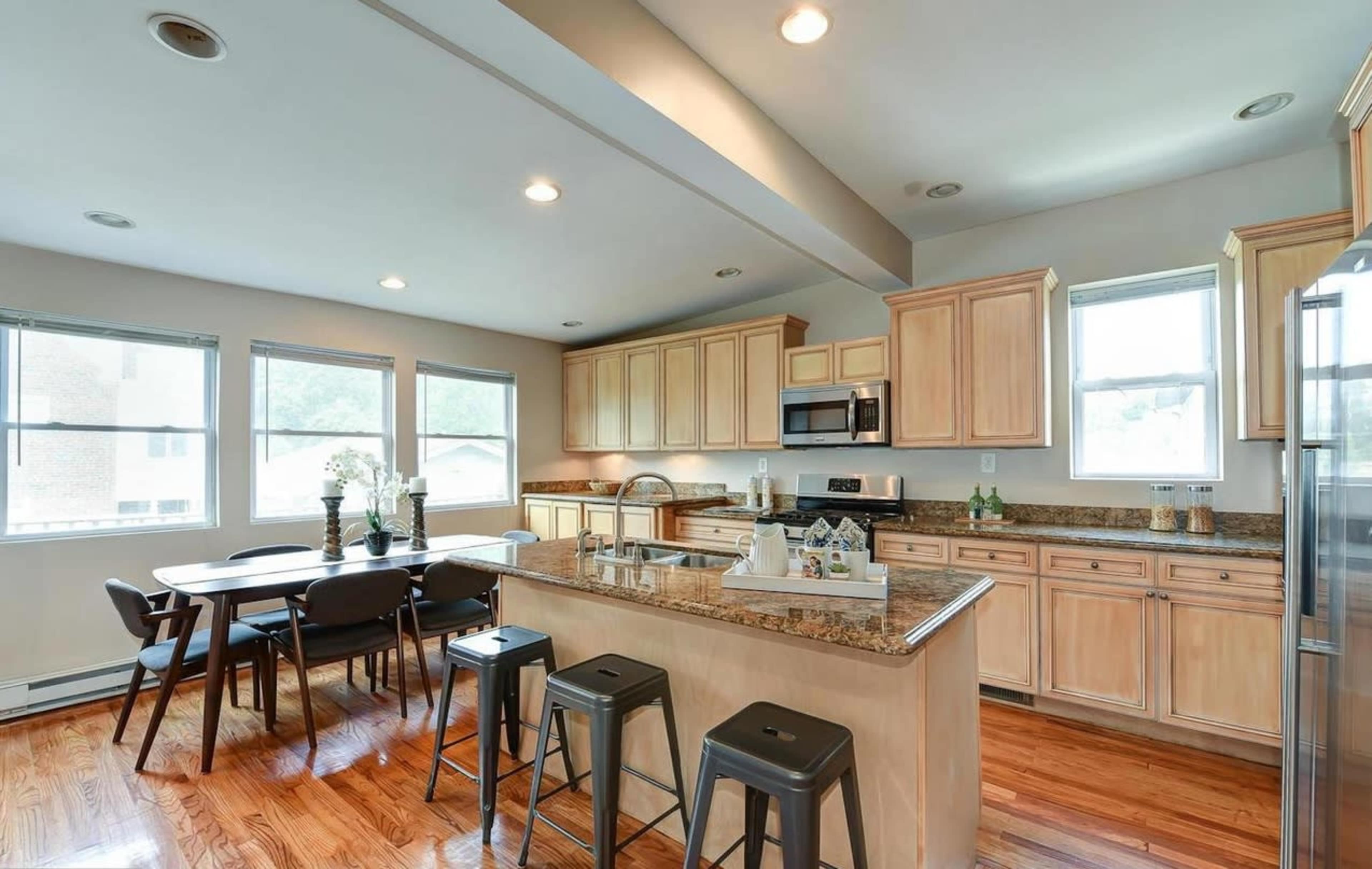 A modern kitchen with wooden cabinetry, a granite countertop, a center island with bar stools, and a dining table nearby.