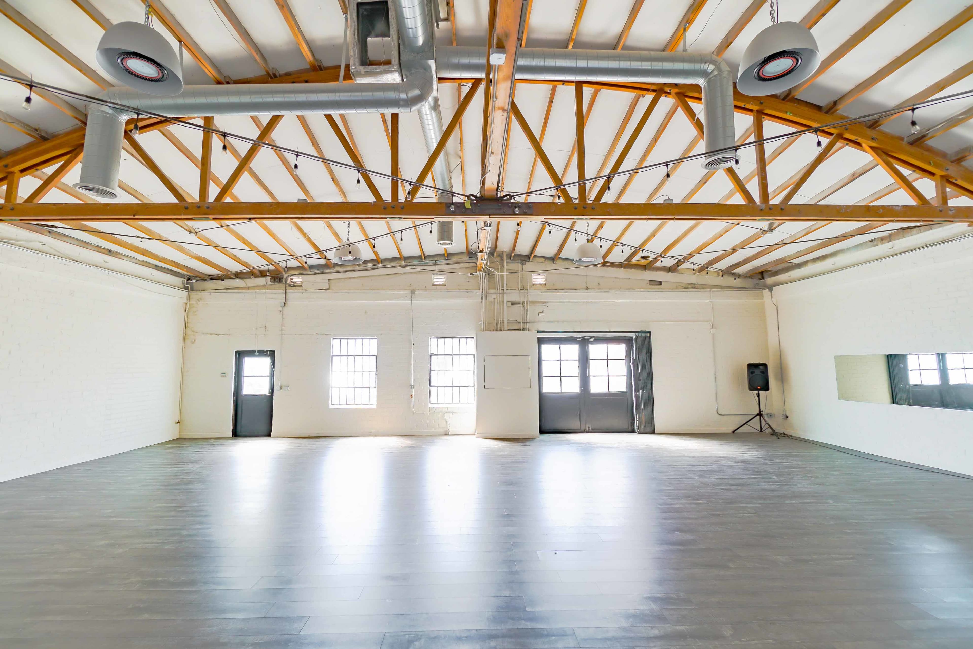 An empty, spacious interior with wooden beams, large windows, and mirrored walls.