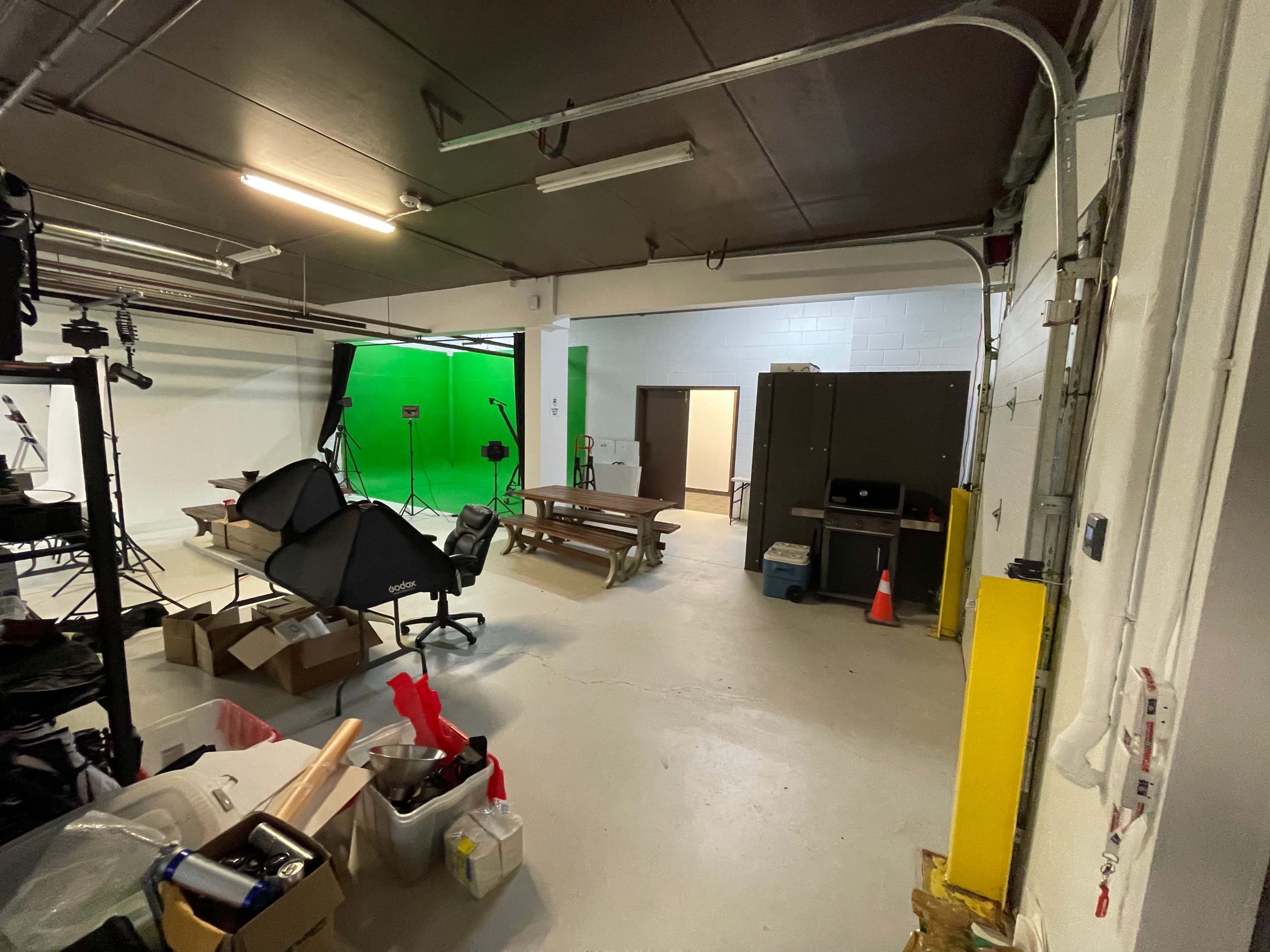 A spacious room with a green screen setup, various equipment on the floor, and a storage area in the back.