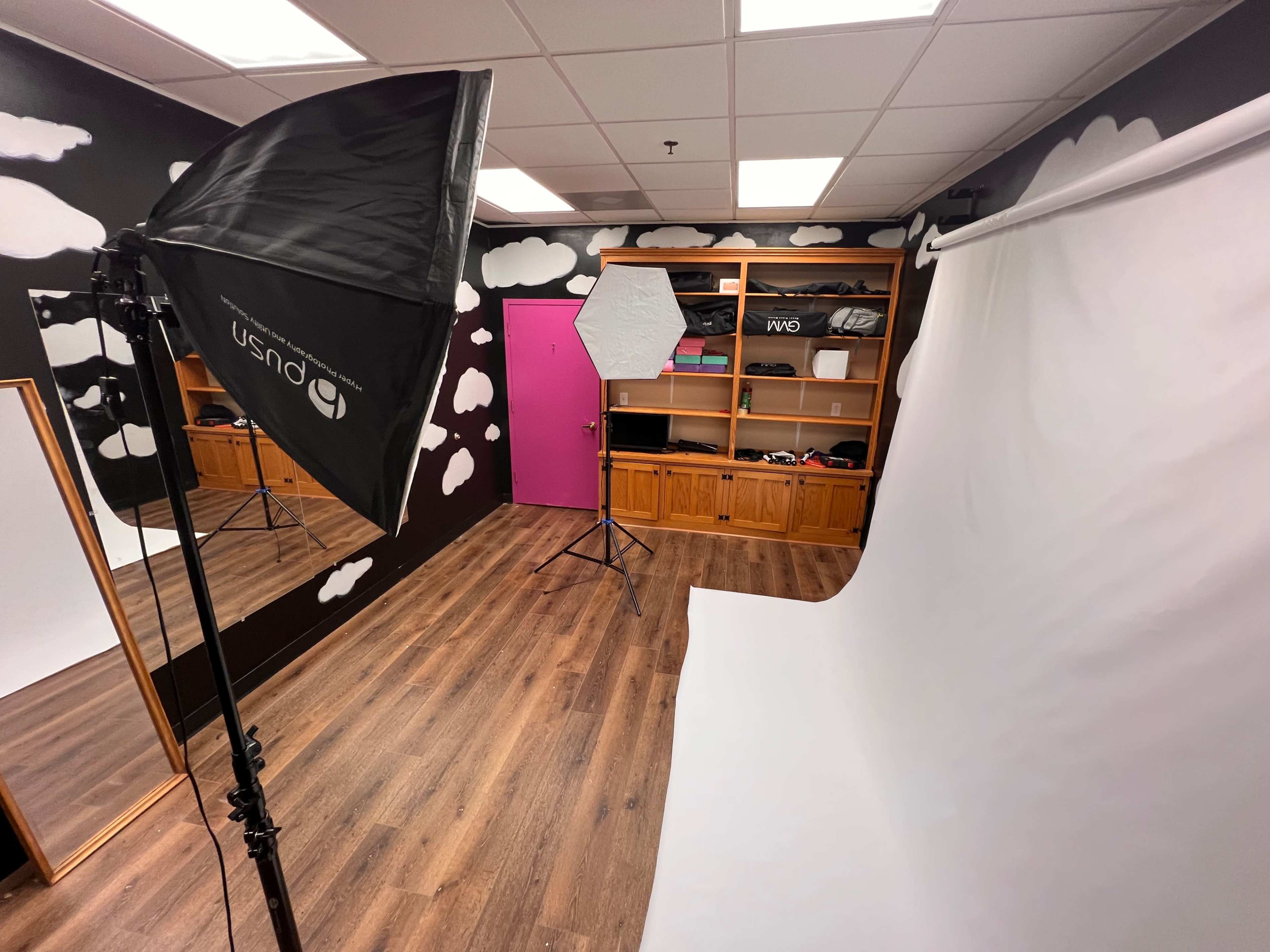 The image shows a photography studio with a backdrop, lighting equipment, and shelves filled with various items.