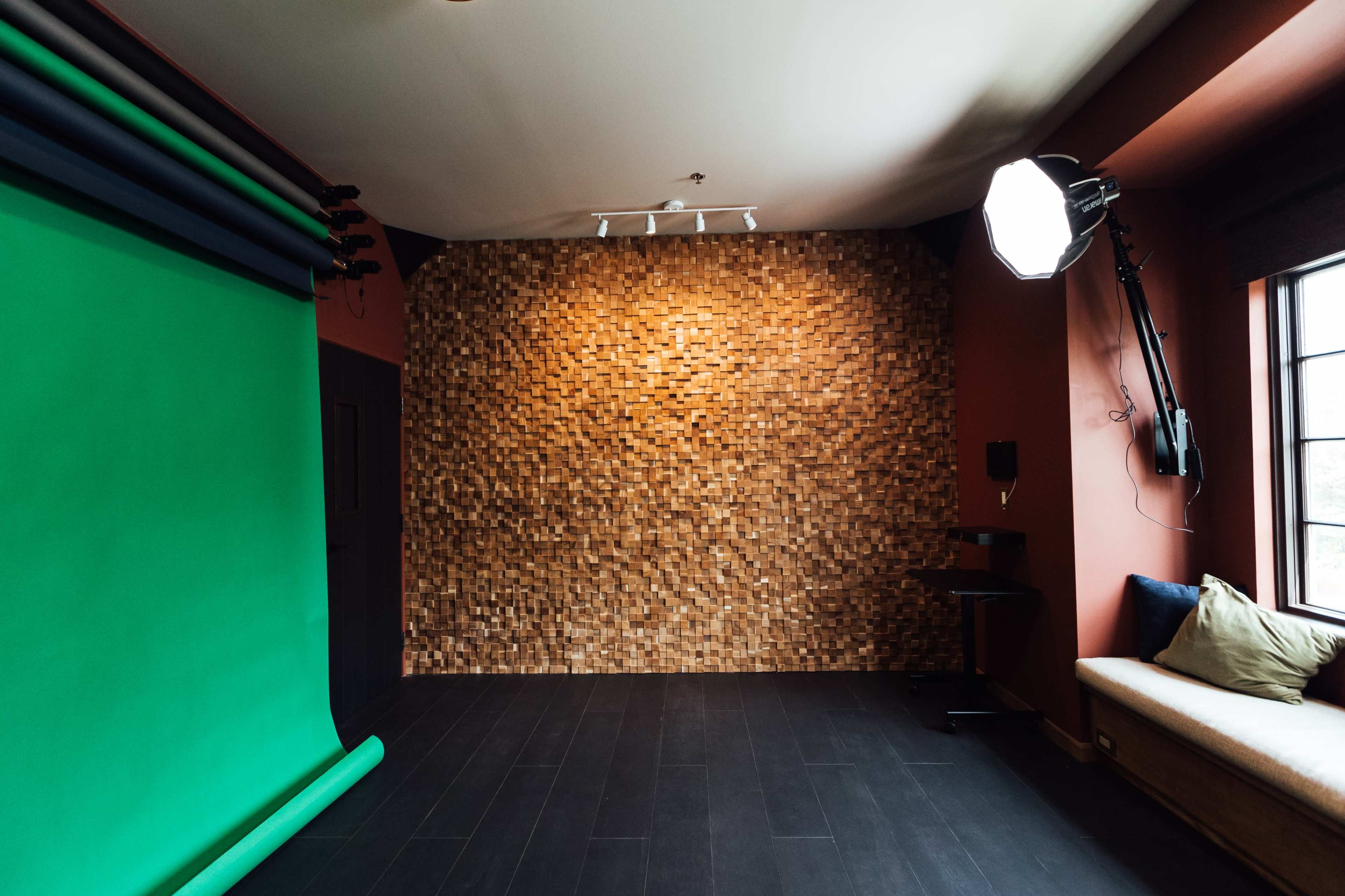 A photo studio with a green screen on the left side and a textured wooden wall in the background, along with a softbox light mounted on the wall and a couch on the right.