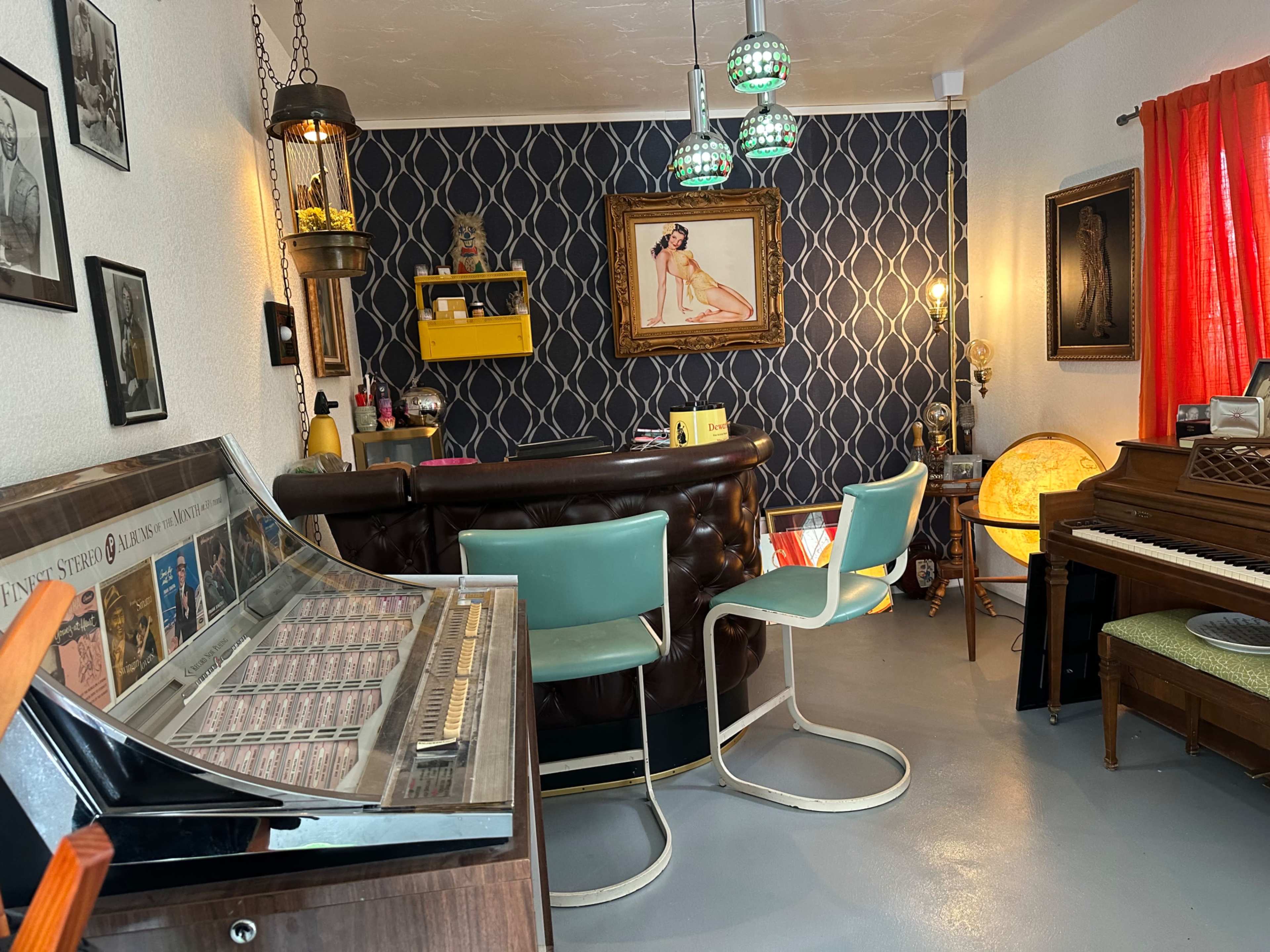The image shows a retro-styled room featuring a jukebox, two bar stools, a piano, and colorful decorations on the walls.