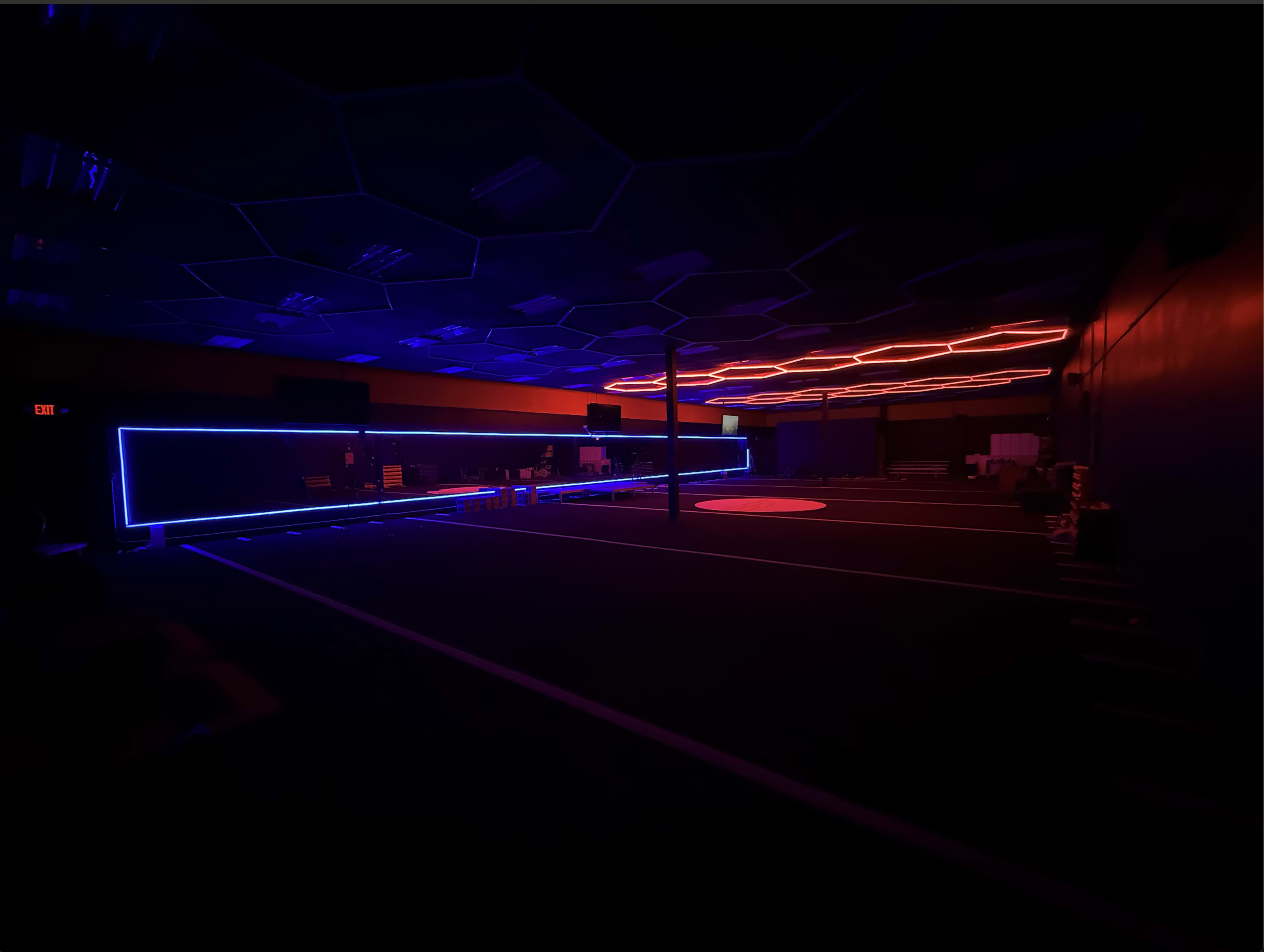 The image shows a dimly lit indoor space with glowing blue and red LED lights outlining the walls and floor.