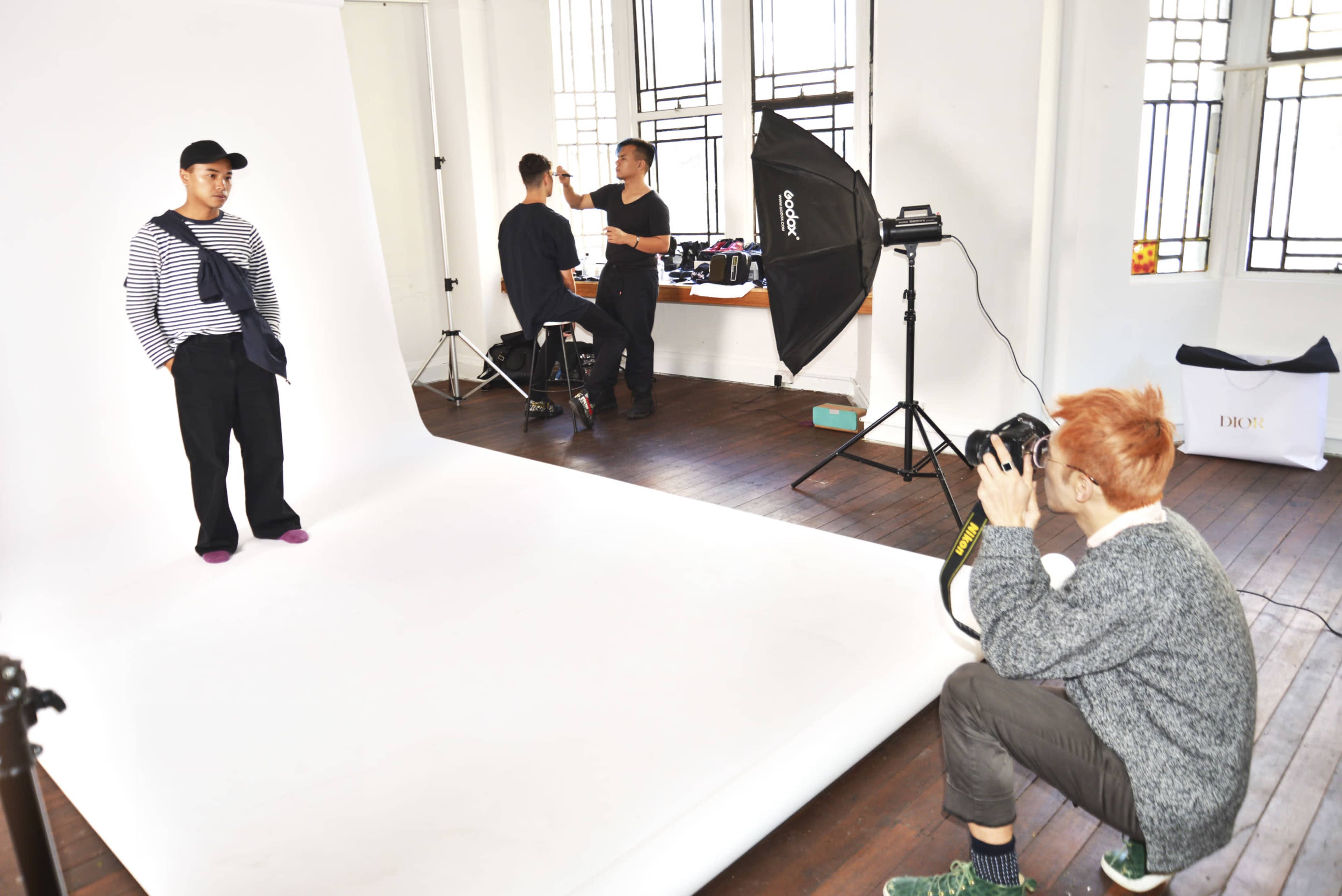 A photographer captures a model posing in a studio while another person adjusts equipment.