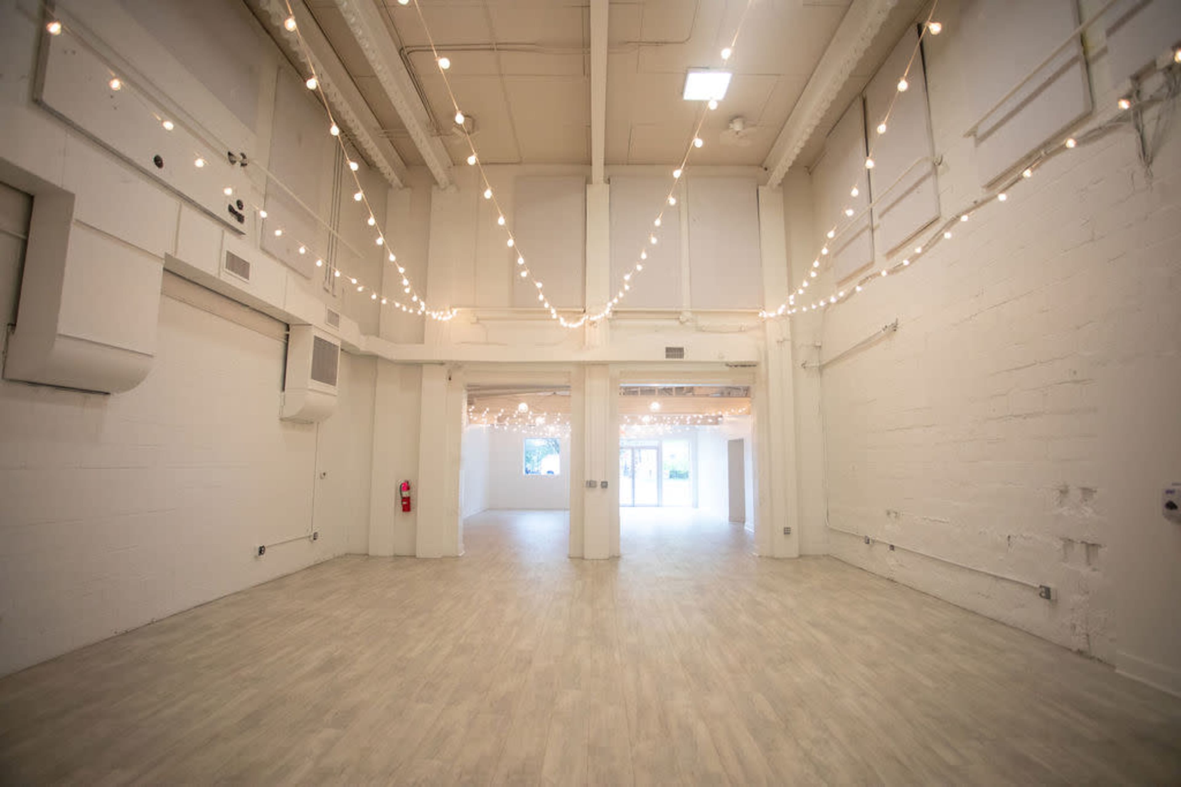 A spacious, well-lit room with white walls and string lights hanging from the ceiling.