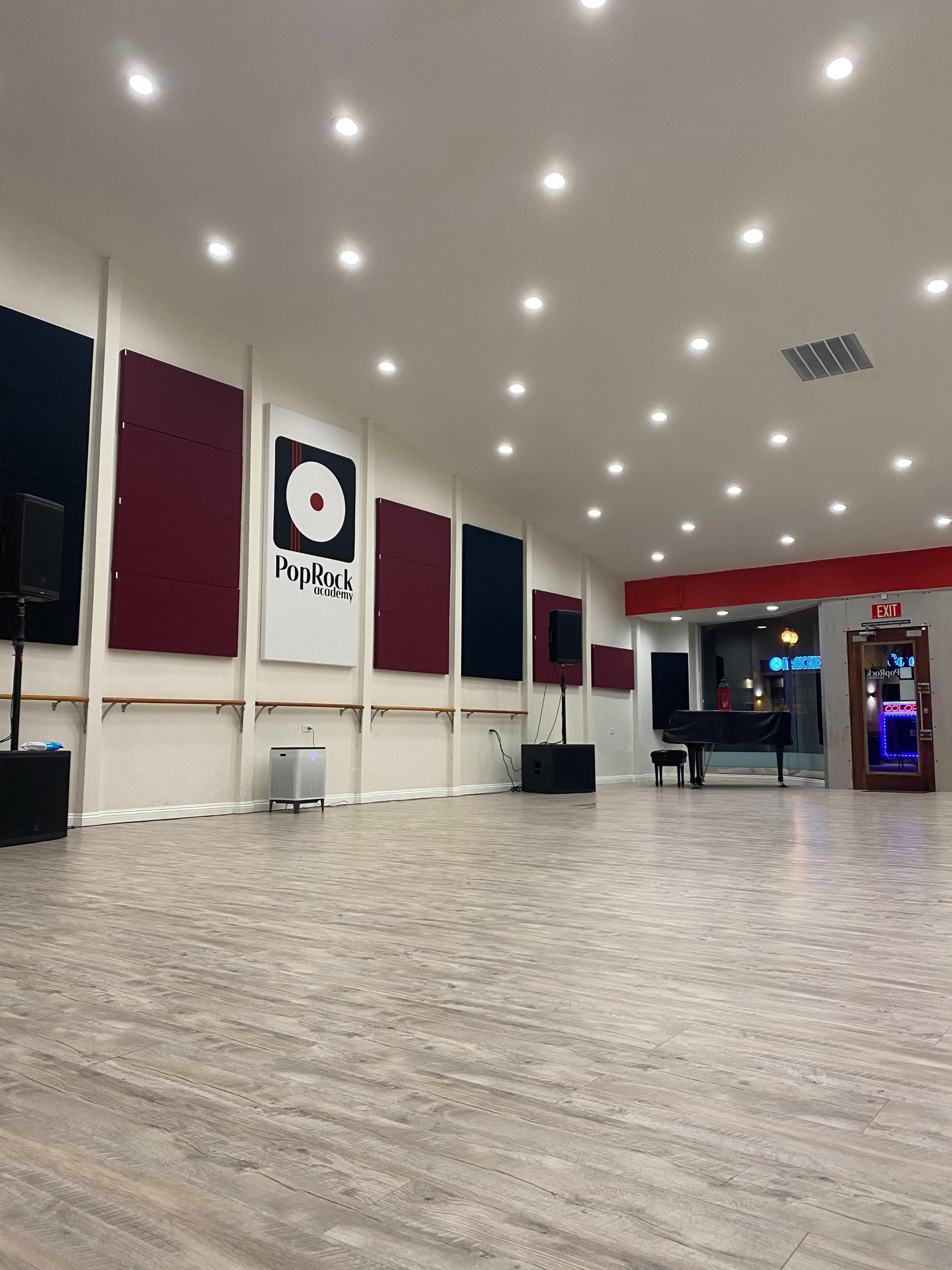 An empty music studio with a wooden floor, featuring a large logo on the wall and soundproofing panels around the room.