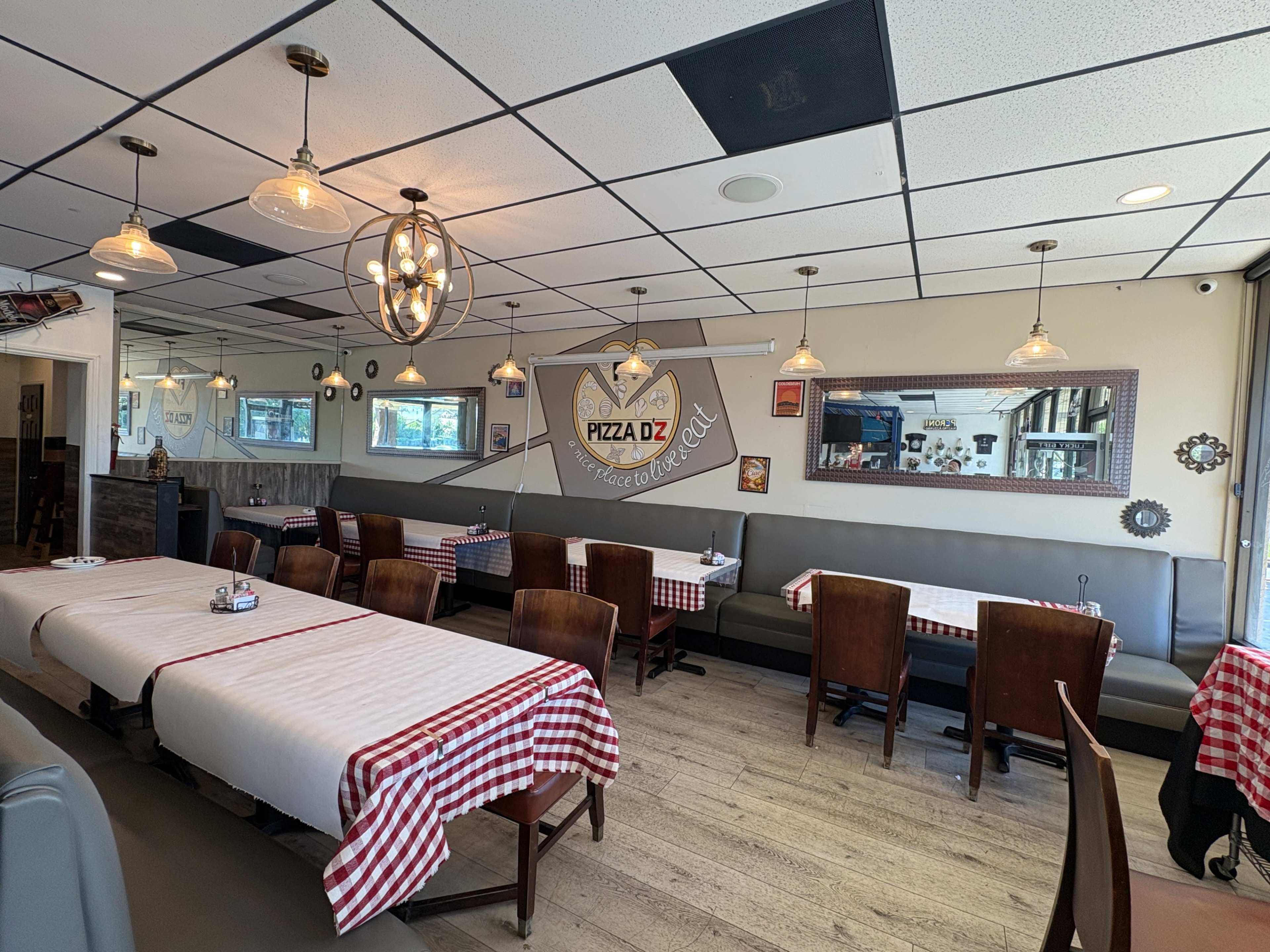 The image shows an interior view of a restaurant with tables covered in red-checked tablecloths, wooden chairs, and pendant lighting.