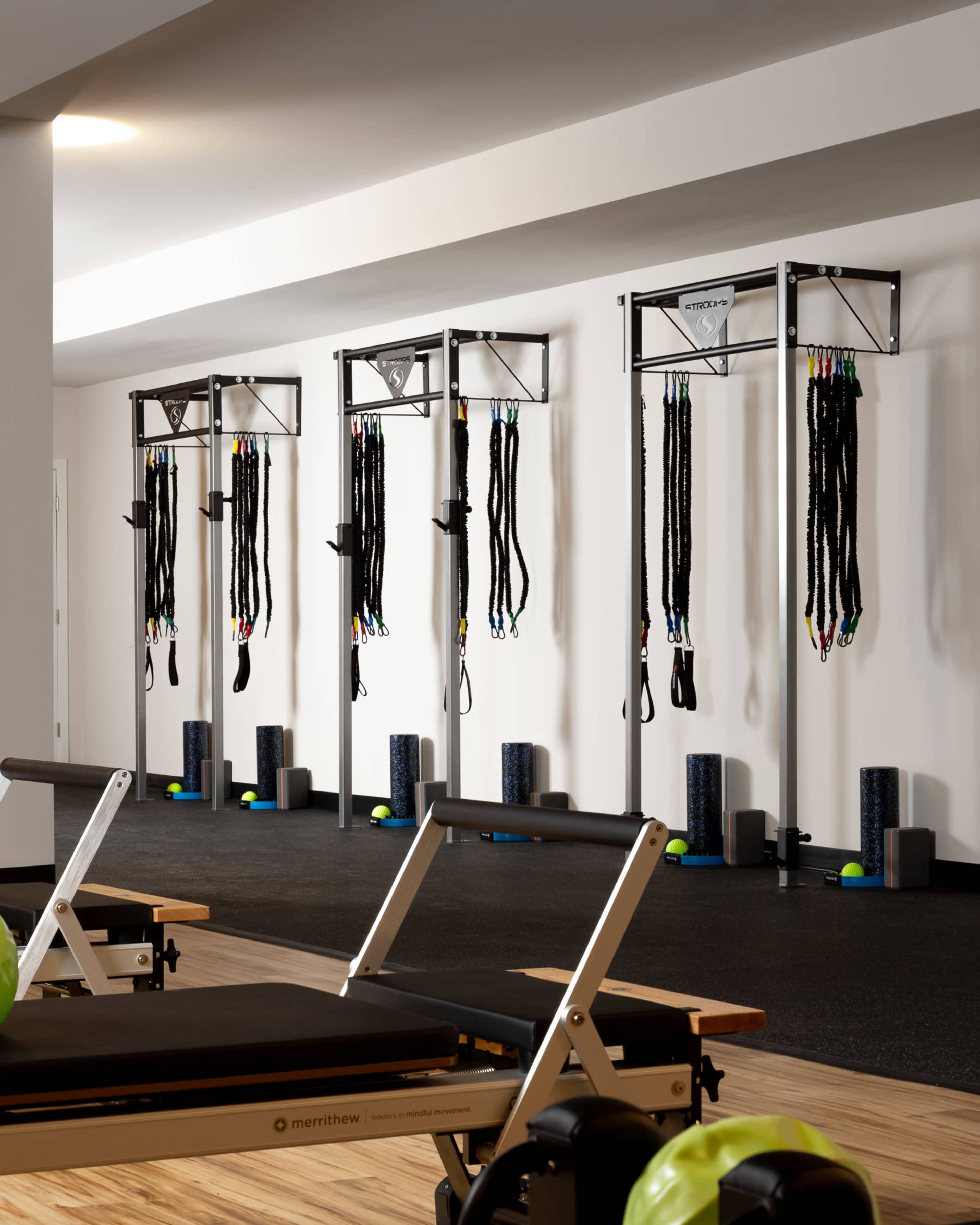 The image shows a fitness studio equipped with multiple vertical wall-mounted exercise cables and foam rollers arranged neatly on the floor.
