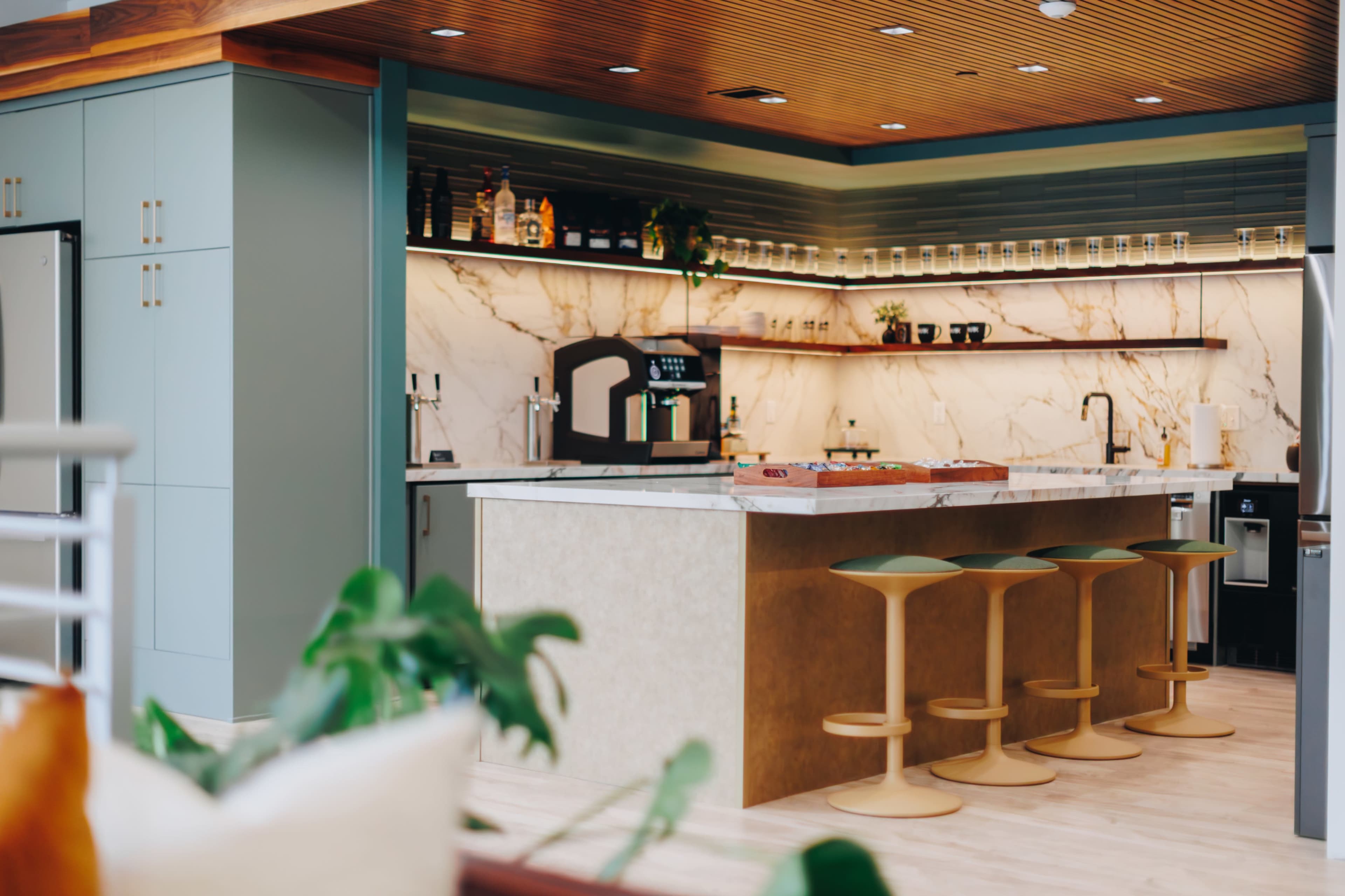 The image shows a modern kitchen with a marble backsplash, a large island with bar stools, and organized shelves displaying various bottles and kitchenware.