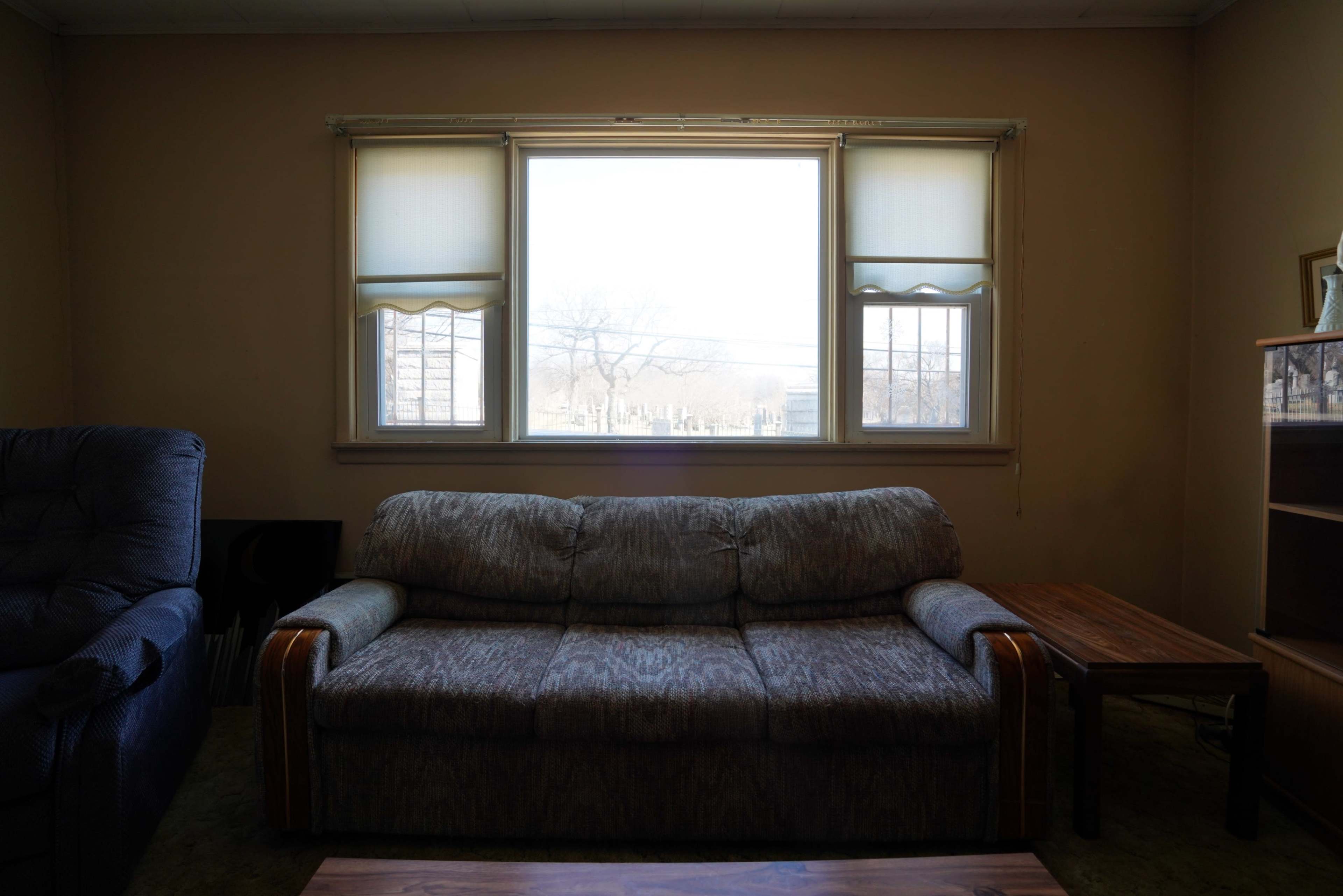 A living room with a couch facing a large window, a small table beside it, and a bookshelf in the corner.