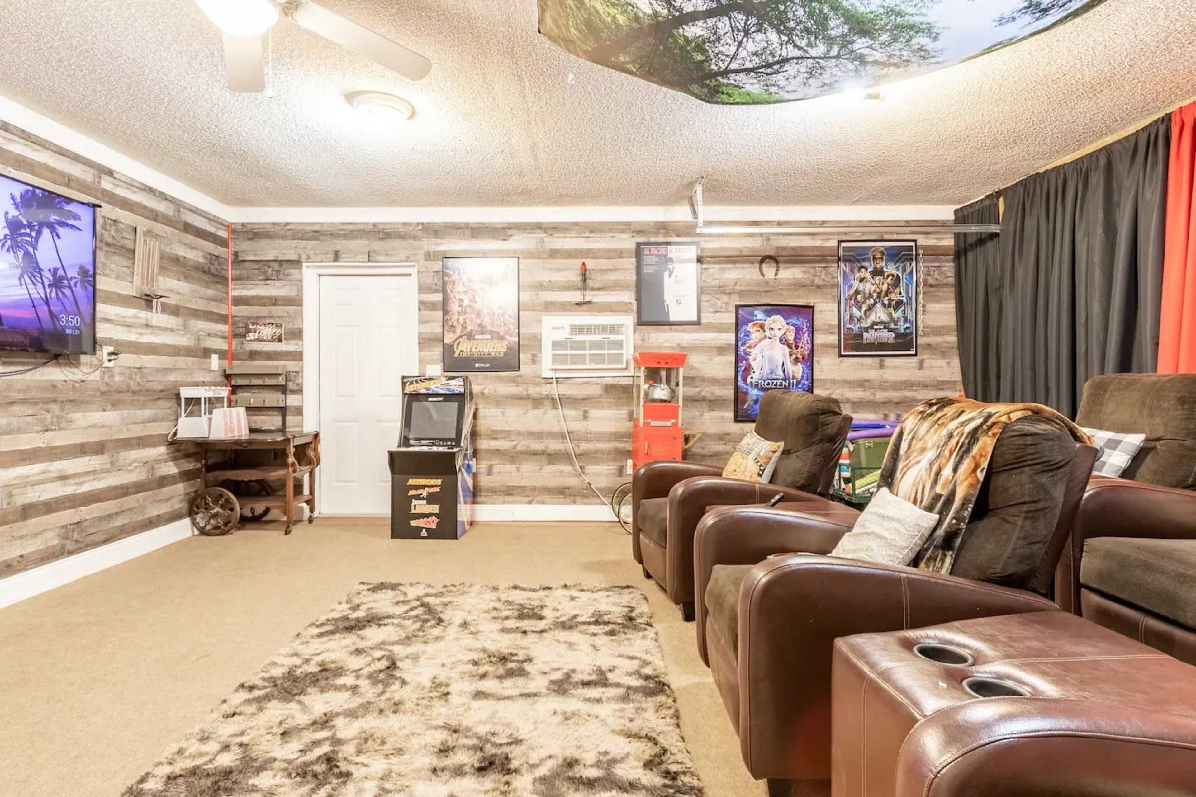 The room features a home theater setup with plush brown recliners, a large screen on the wall, and decorative movie posters.