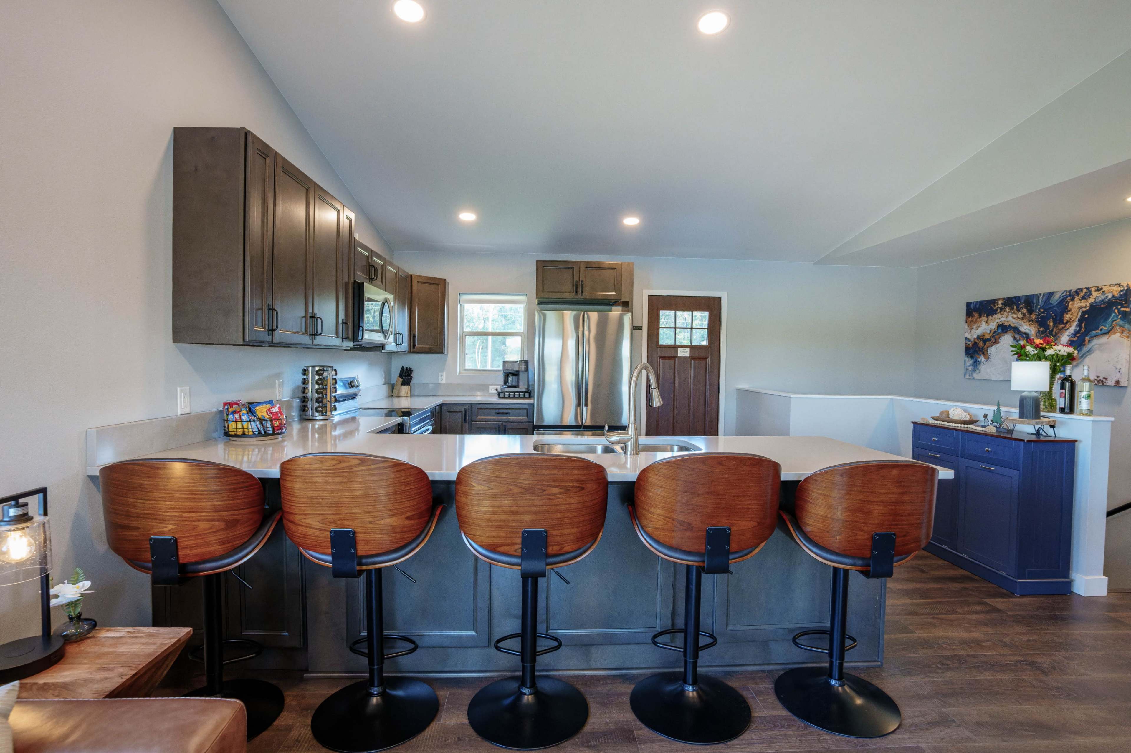 The image shows a modern kitchen with a large island featuring four high-backed stools and stainless steel appliances.