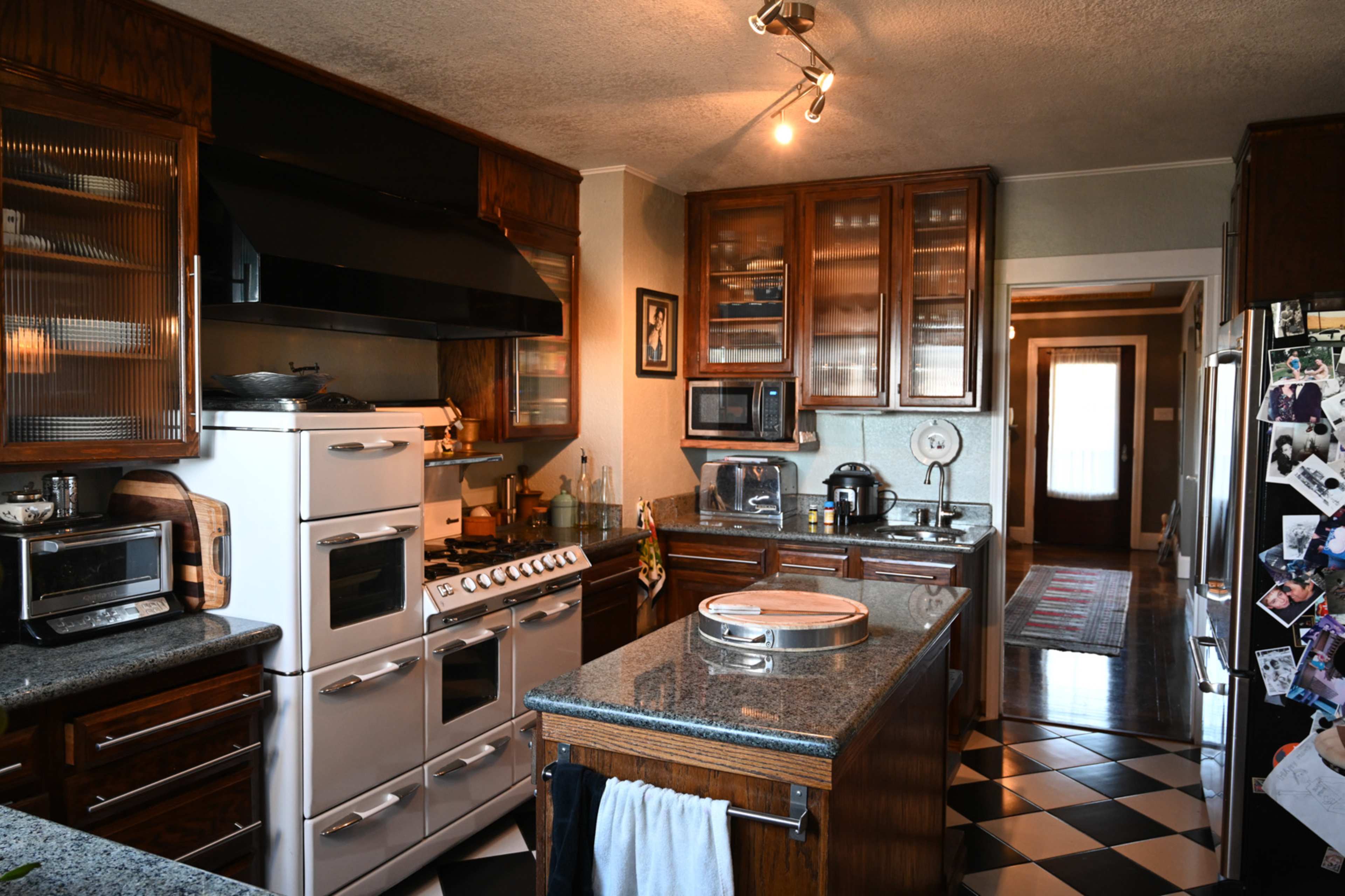 The kitchen features dark wood cabinets, a stainless steel refrigerator, and a mix of black and white checkerboard flooring.