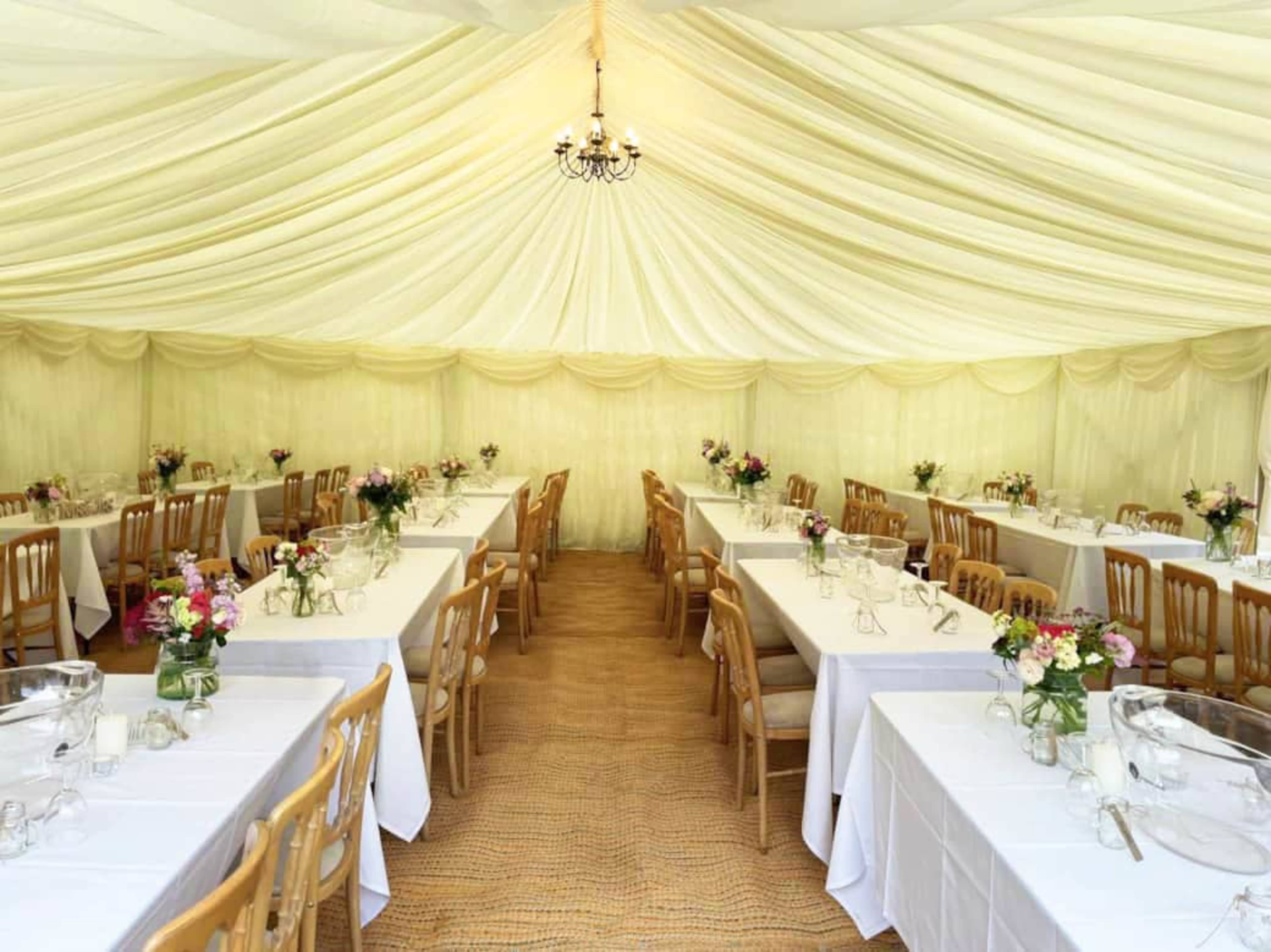 A large, elegantly arranged tent features several long tables with white tablecloths and floral centerpieces.