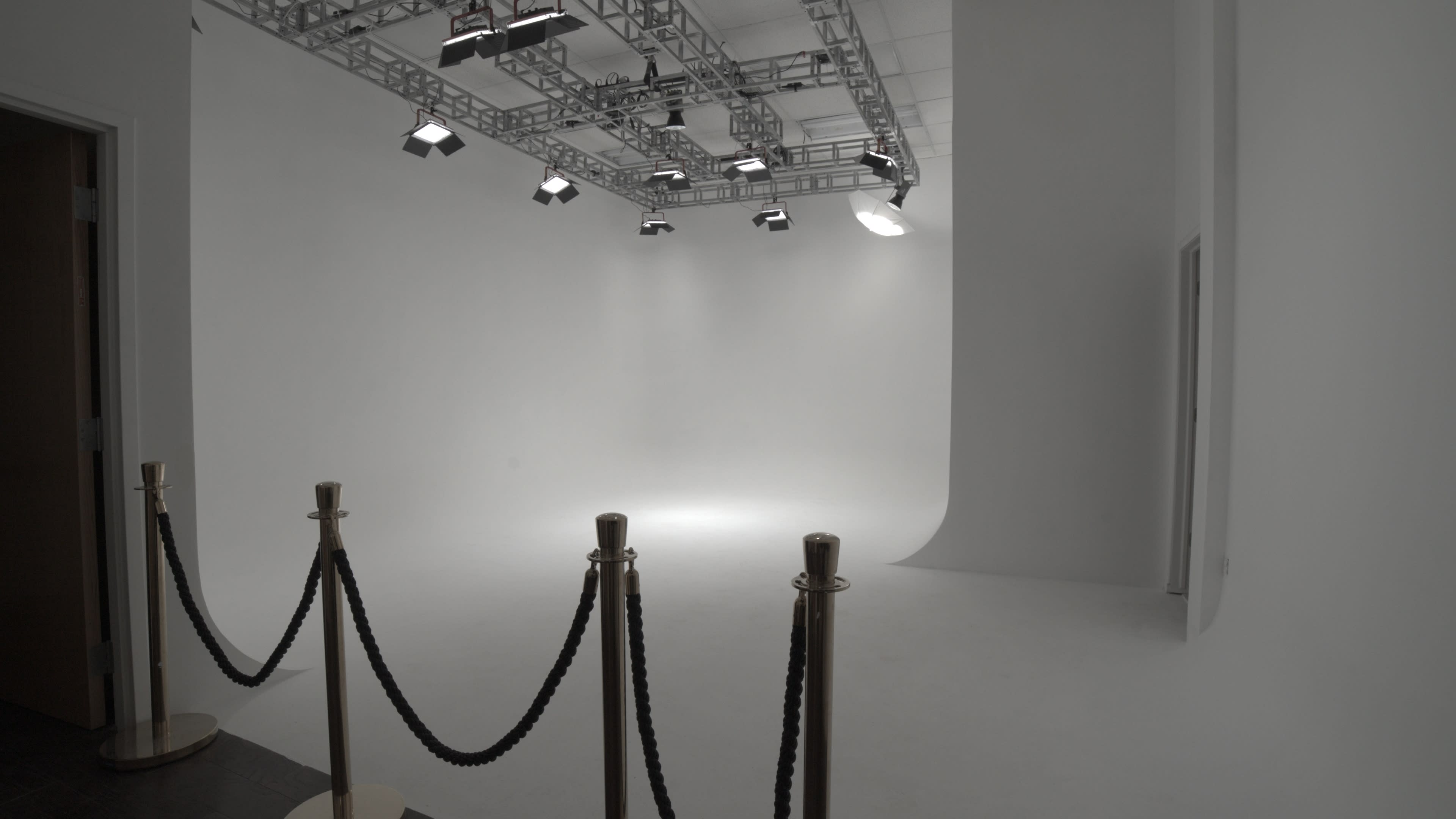 A spacious, empty studio with a seamless white backdrop, lighting rigs, and a velvet rope barrier at the entrance.
