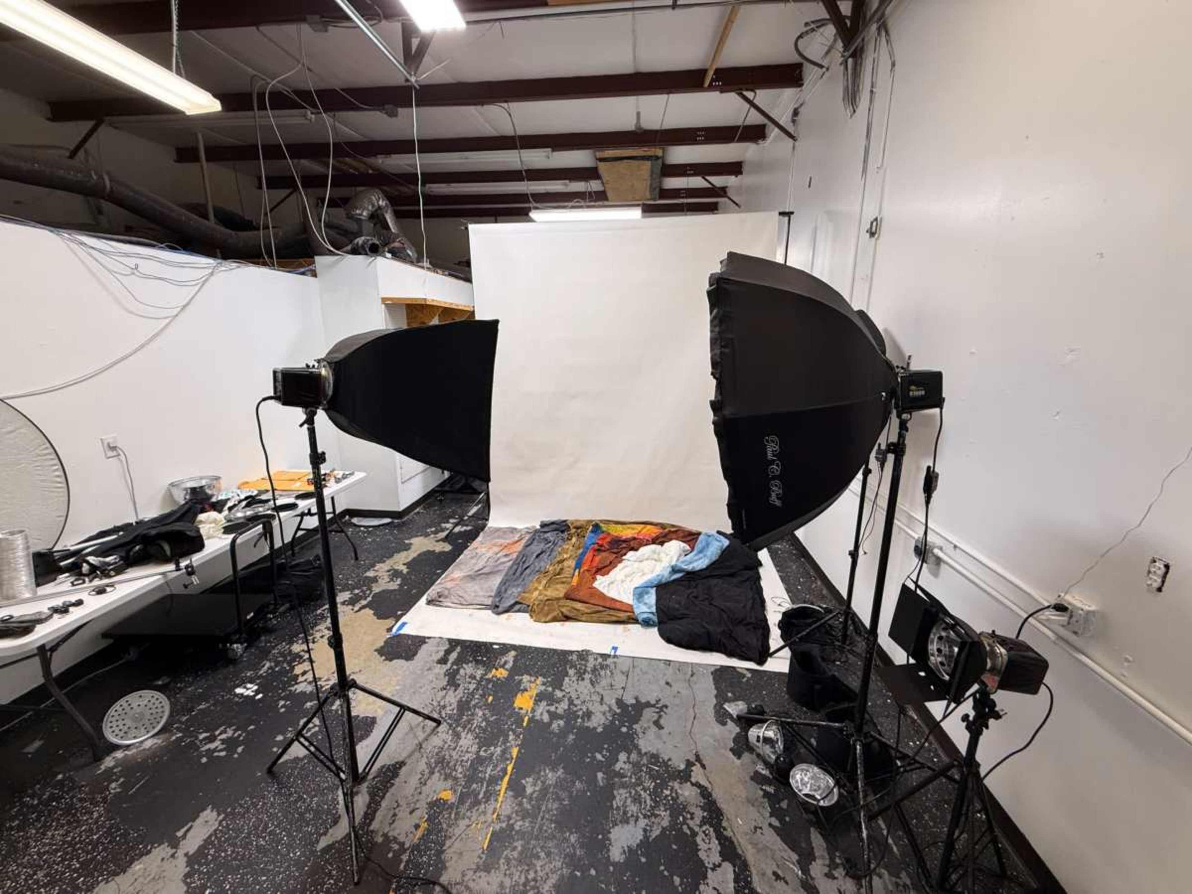 The image shows a photography studio setup with two softbox lights positioned to illuminate a wrinkled fabric backdrop on the floor.