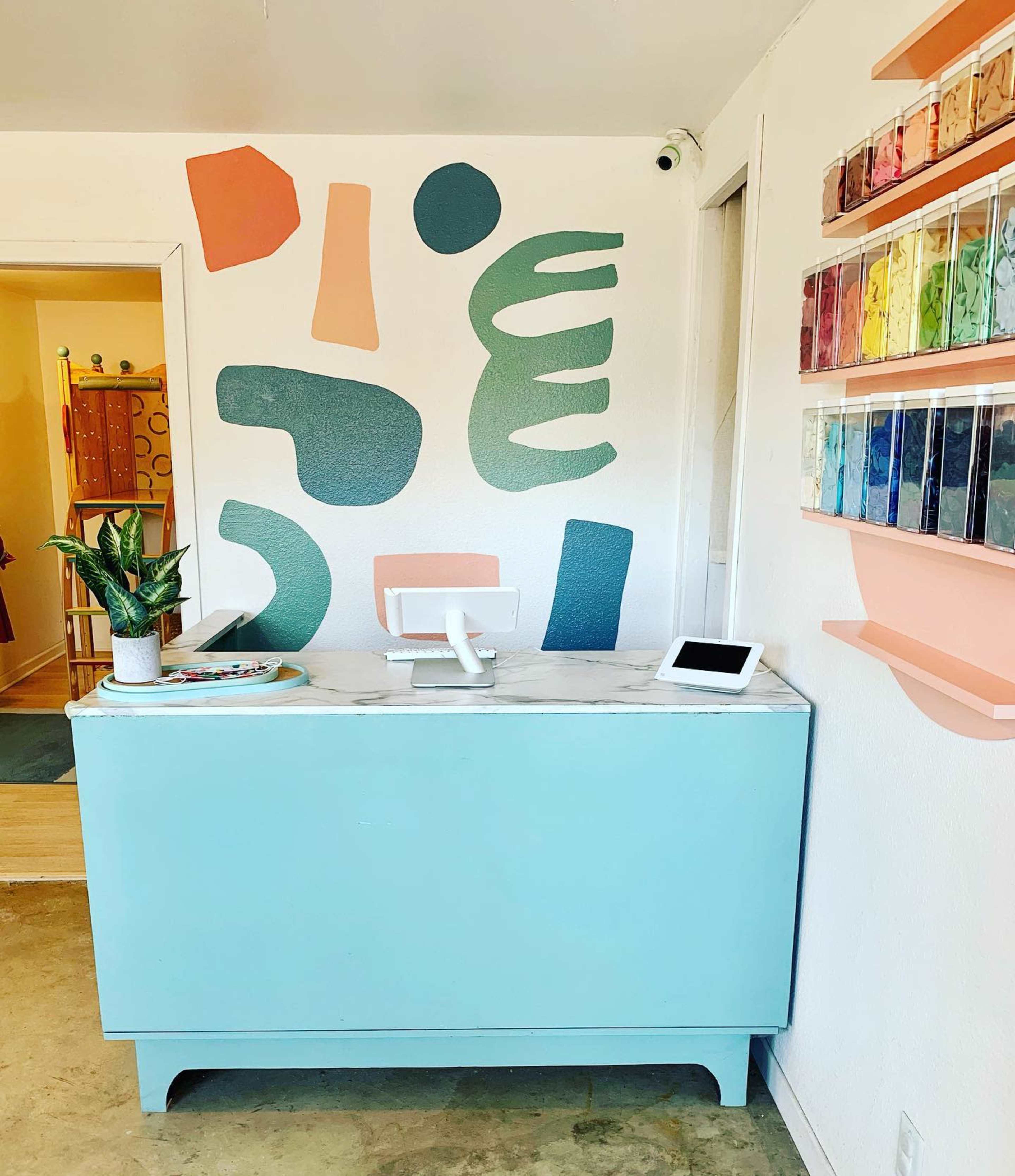 A reception area with a turquoise counter, a digital payment station, and a colorful abstract mural on the wall.