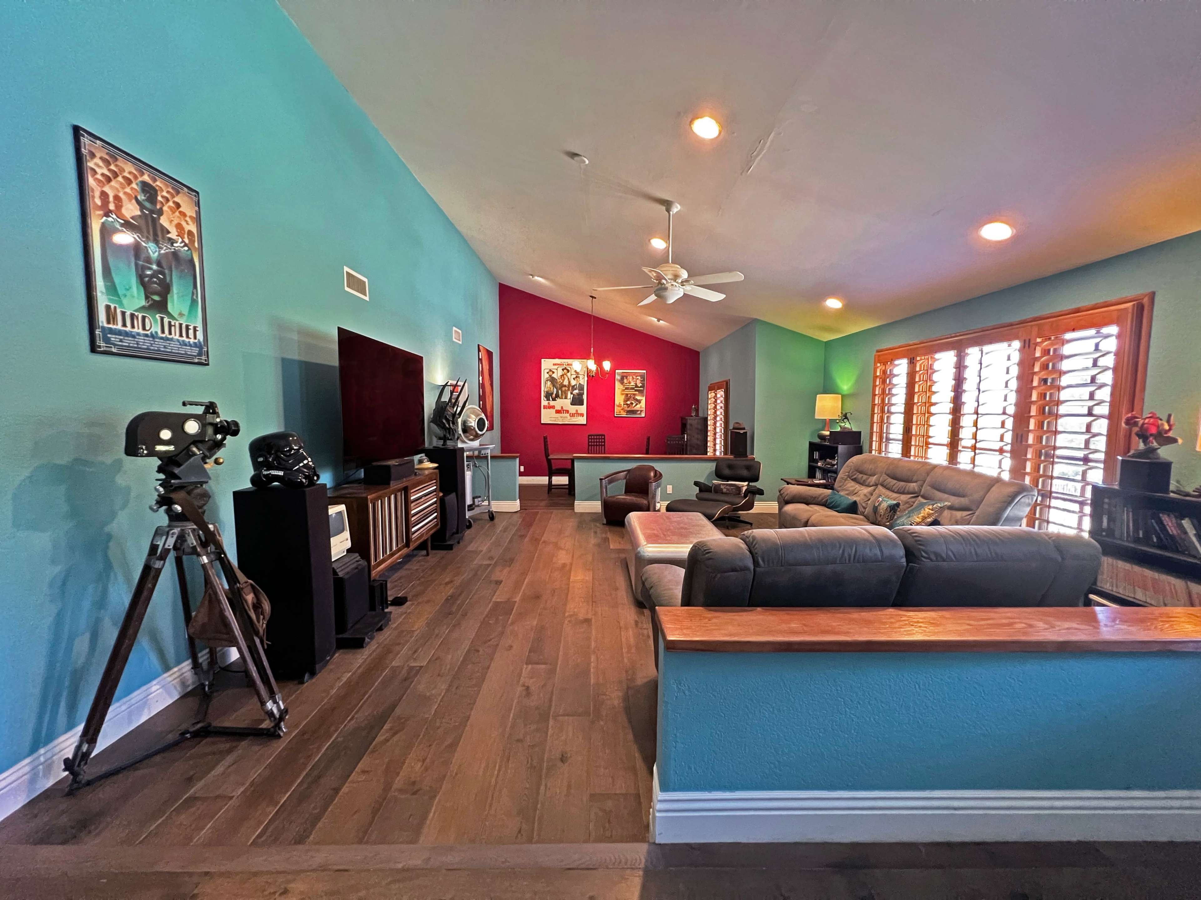 The room features a spacious living area with a teal accent wall, a large television, comfortable seating, and decorative movie posters.