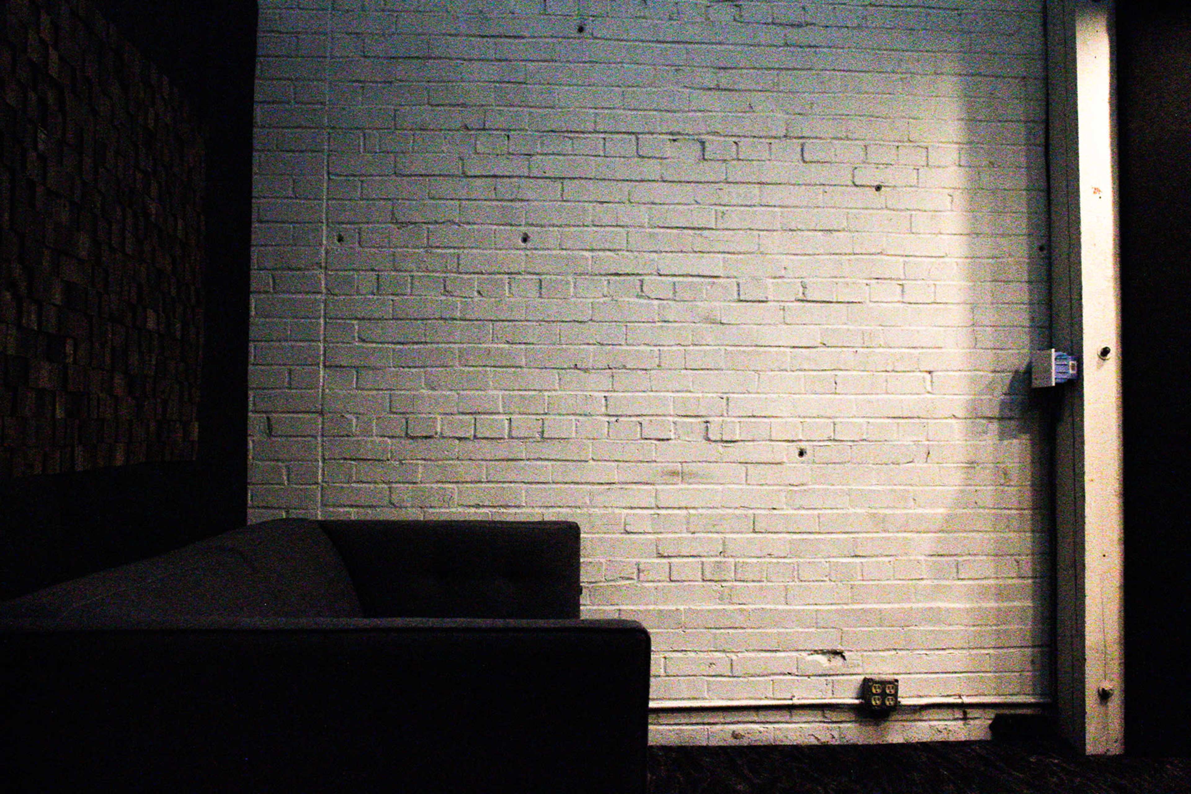 A gray couch is positioned against a white brick wall in a dimly lit room.